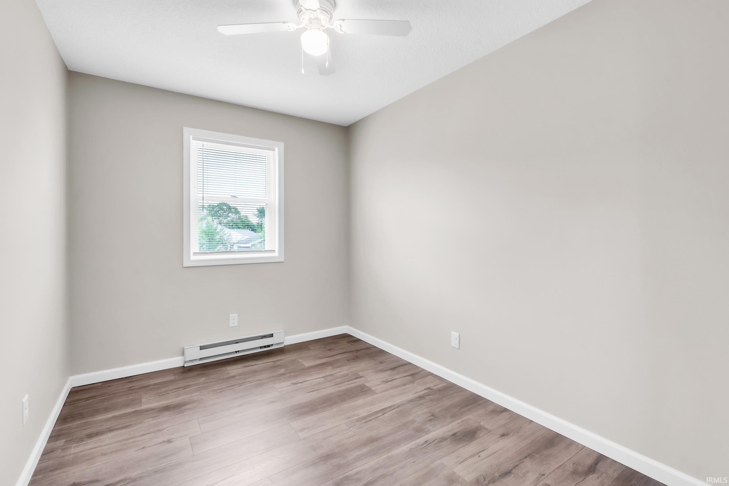 Spacious room featuring wood-finish flooring, light gray wall paint, and white baseboards