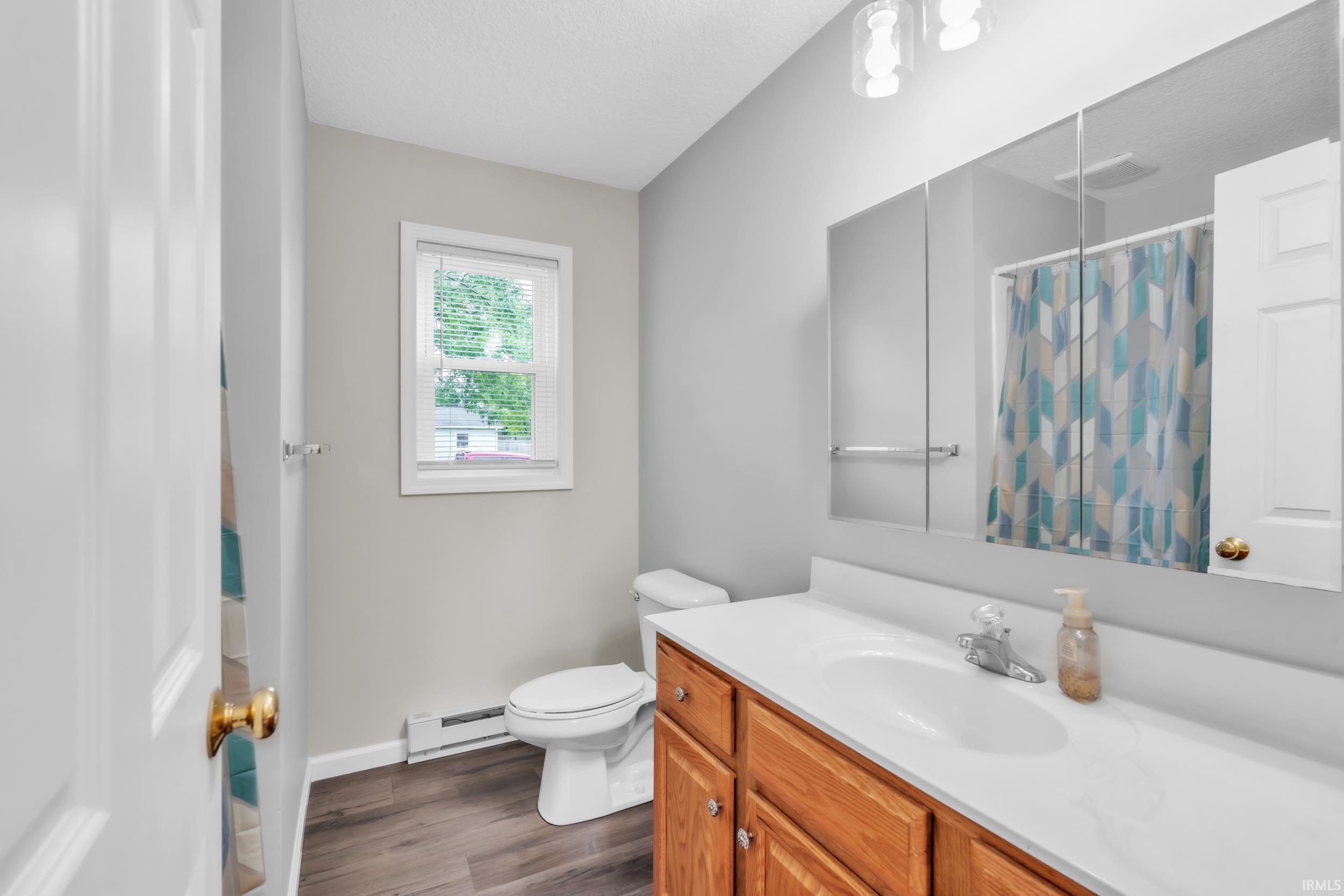 Bathroom featuring a wood-finish vanity with an integrated white sink, a large mirrored medicine cabinet, and wood-look flooring