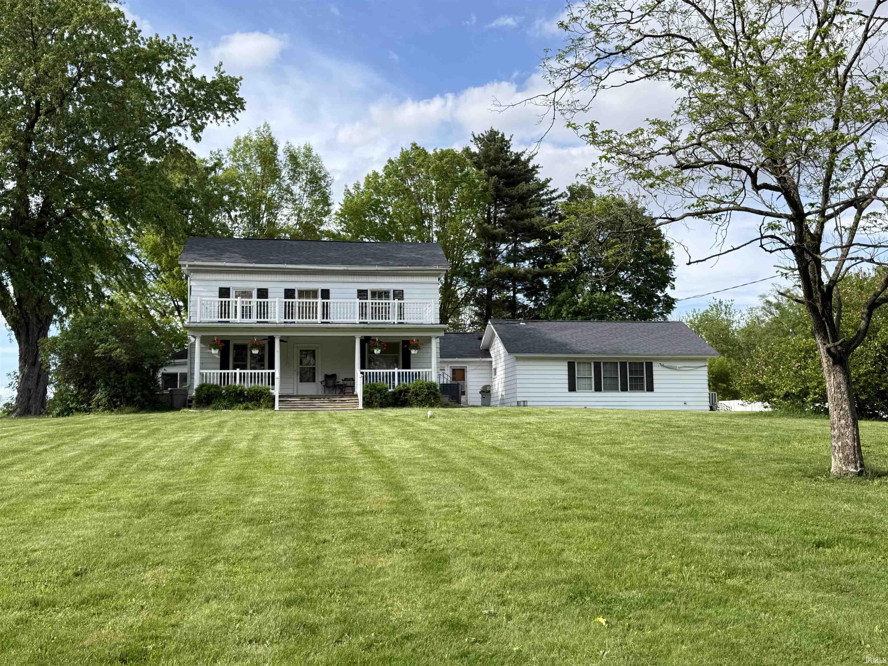 Two-story white residence featuring a full-width covered front porch and an upper-level balcony with white railings