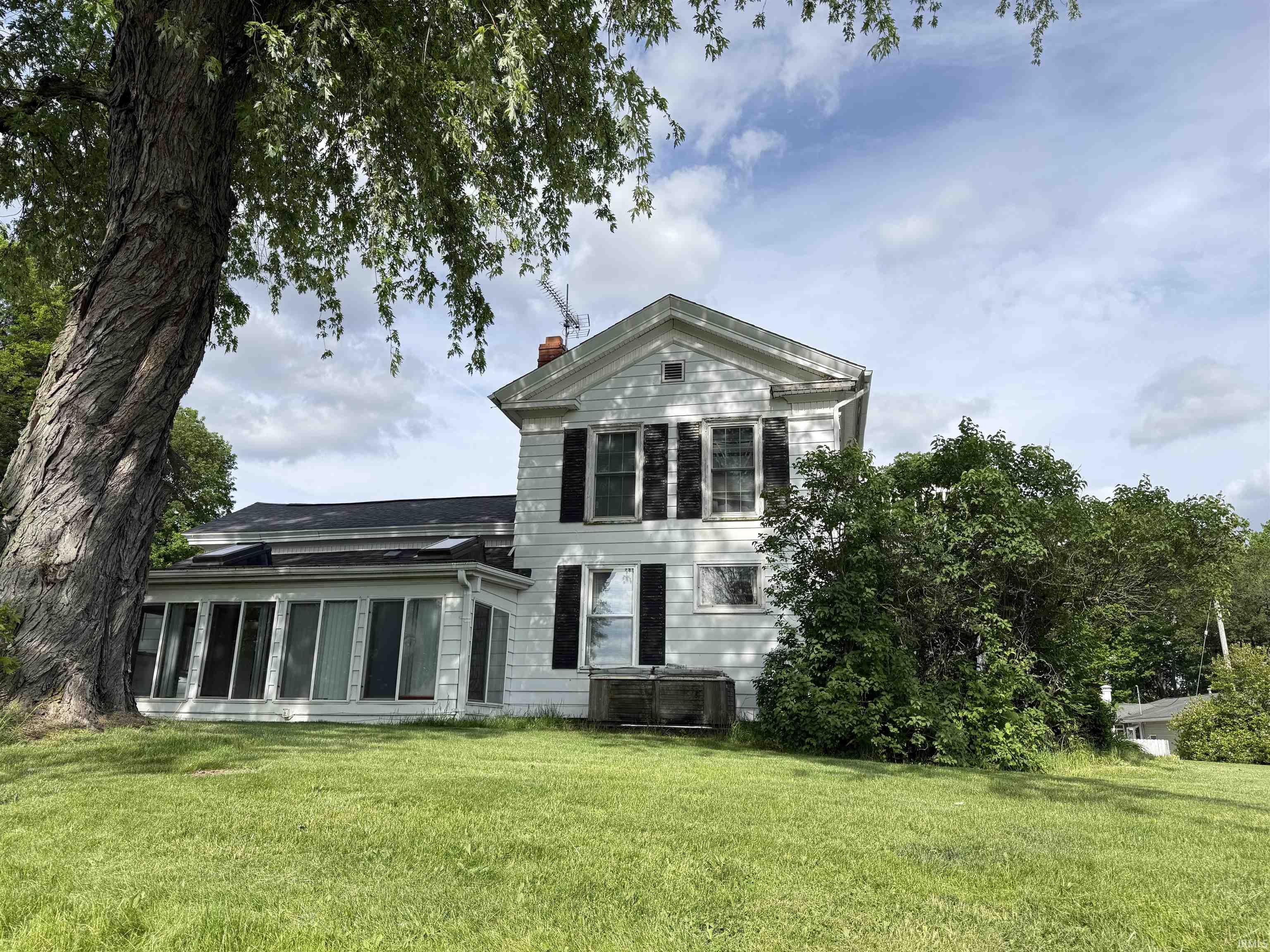 Classic white exterior with dark shutters, featuring a traditional peaked roofline and a red brick chimney