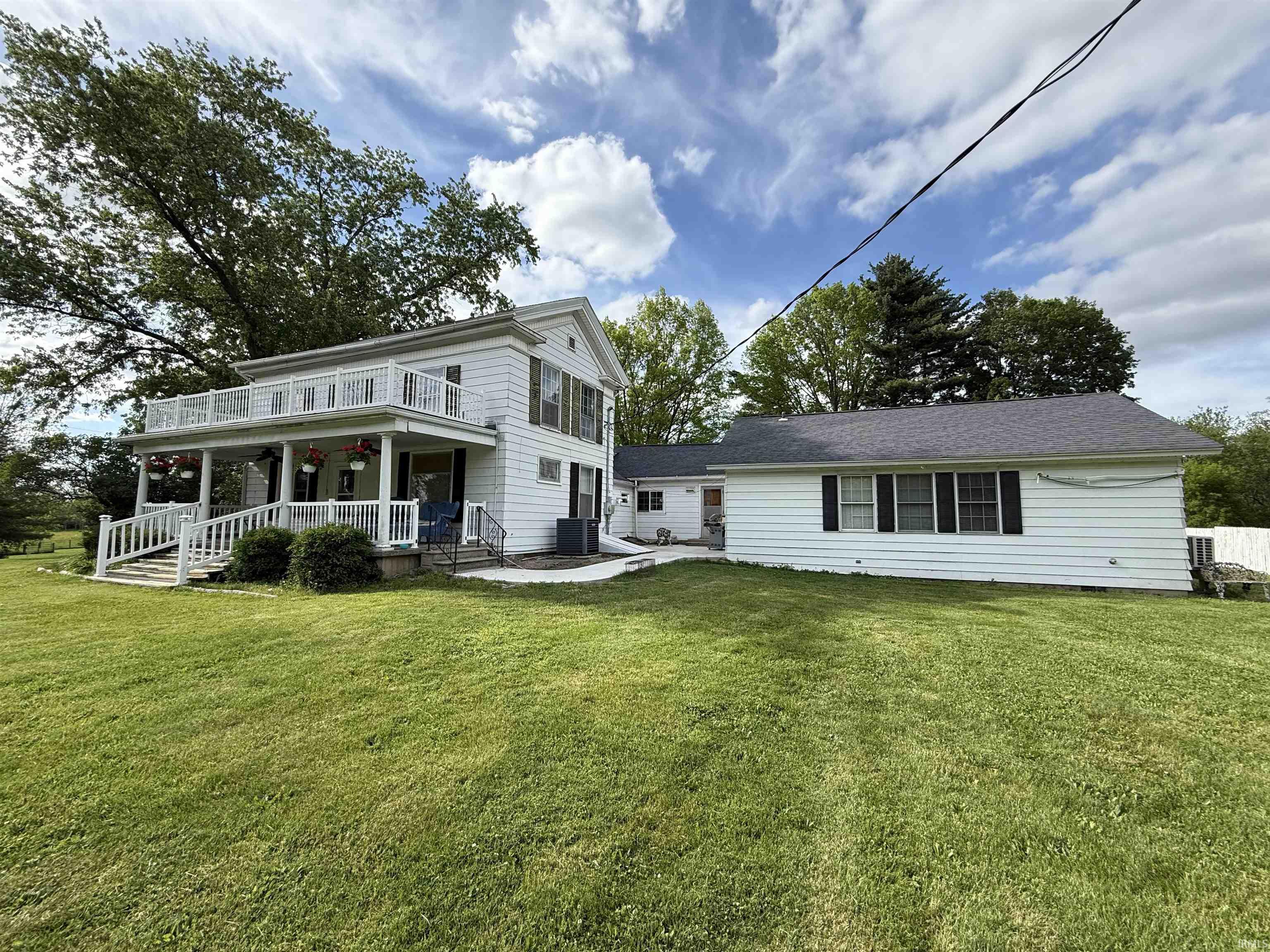 White siding exterior with a full-width covered porch, an upper-level balcony, and a multi-pitch roofline