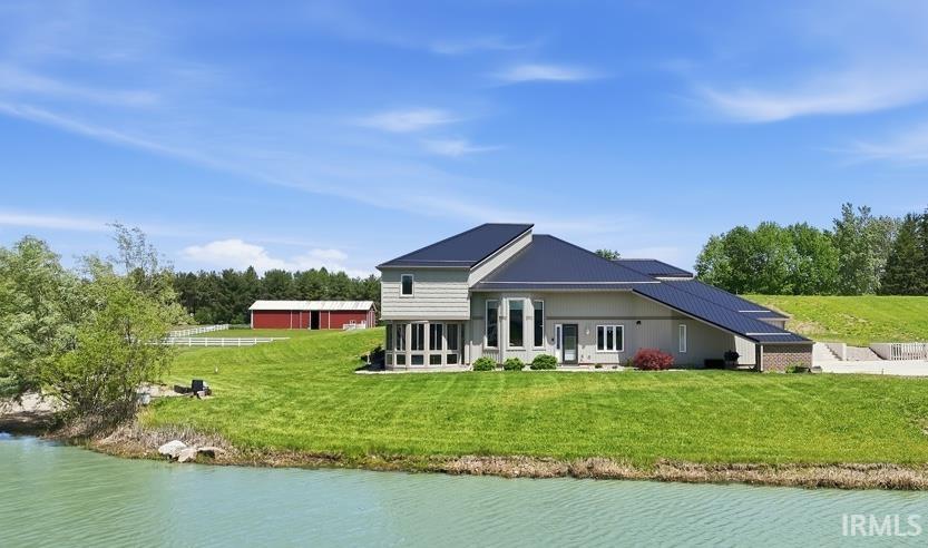 Modern exterior featuring a dark metal roof, light-colored siding, and a prominent pond