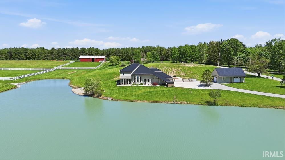 Expansive property featuring a private pond, a substantial residence with a patio, a detached garage, and a red barn structure