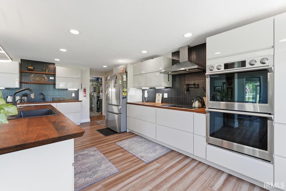 Contemporary kitchen featuring wood-finish flooring, white flat-panel cabinetry, and rich wood countertops