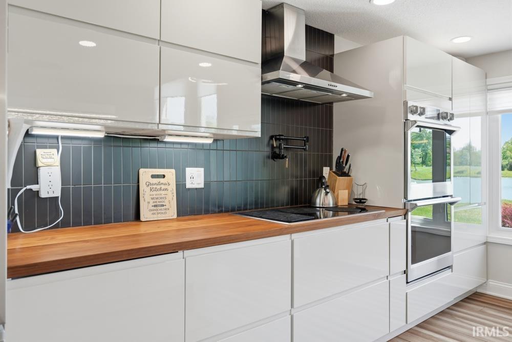 Modern kitchen featuring white flat-panel cabinetry, a wood-finish countertop, and a dark vertical tile backsplash