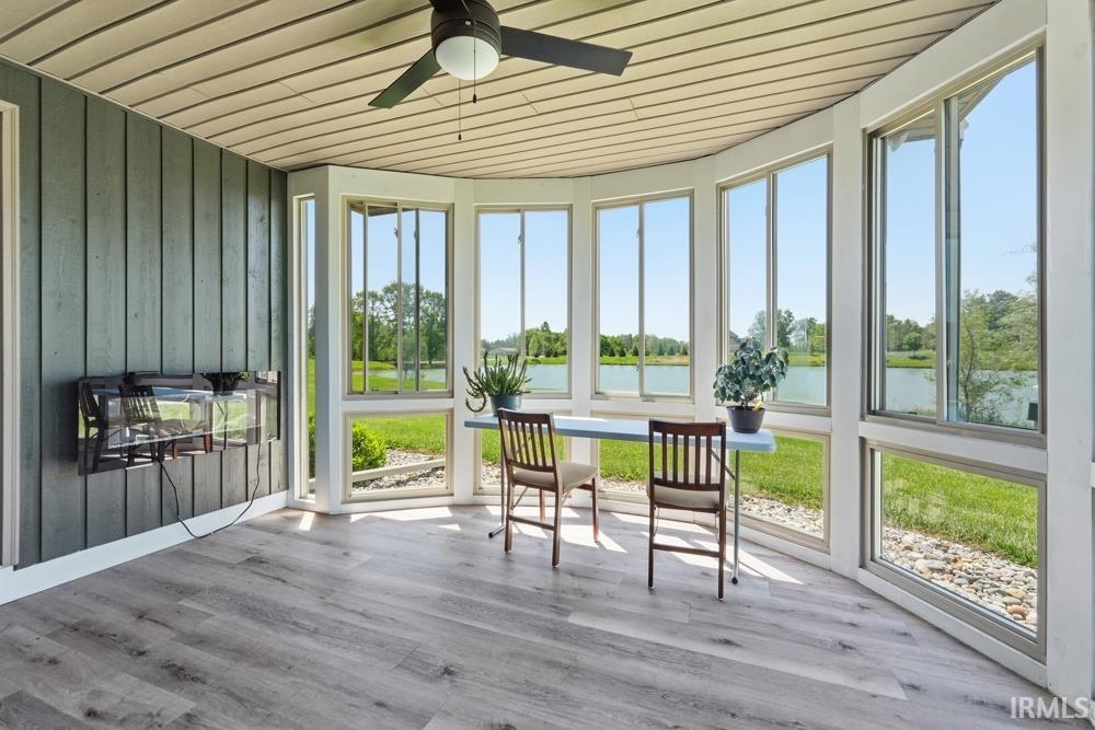 Sunroom featuring expansive windows, wood-finish flooring, a ceiling fan, and a wall-mounted electric fireplace