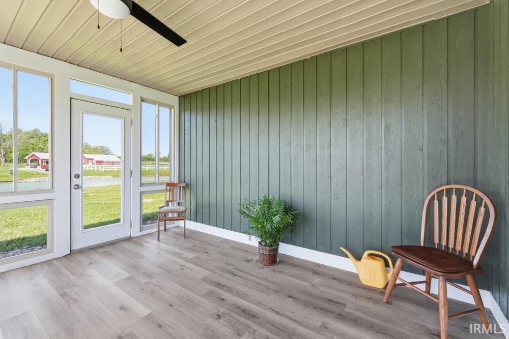 Screened porch featuring light wood-finish flooring, a beadboard ceiling, a ceiling fan, and a green vertical plank wall
