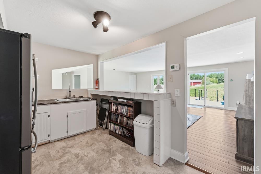 Kitchen area featuring a built-in sink with countertop, white cabinetry, and a pass-through window opening to an additional room with wood-finish flooring