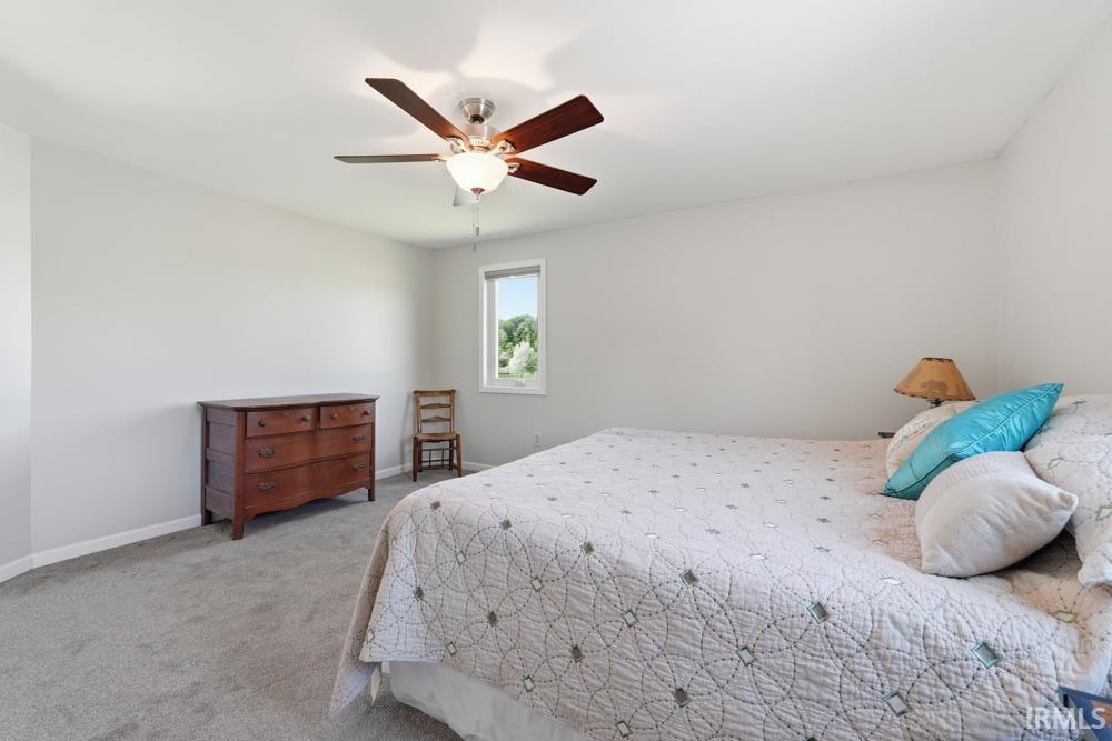 Carpeted bedroom featuring neutral wall tones, a ceiling fan with light fixture, and a window providing natural light