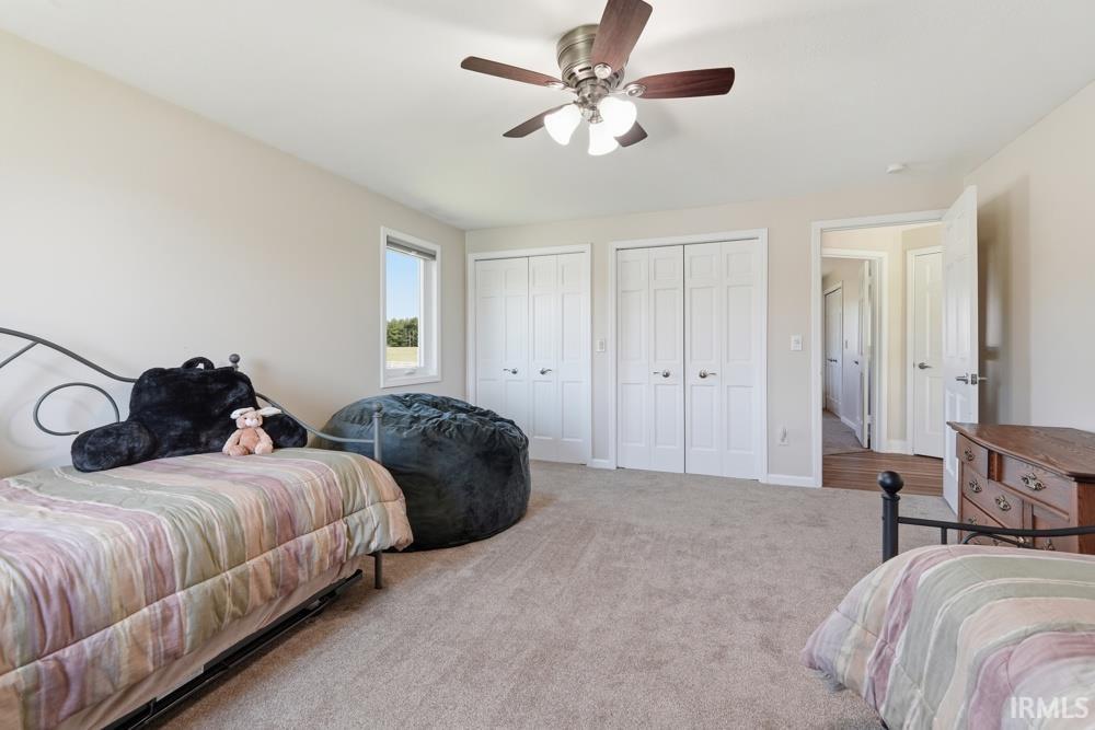 Carpeted room with a ceiling fan, two white bi-fold closet doors, a single window, and a white interior door