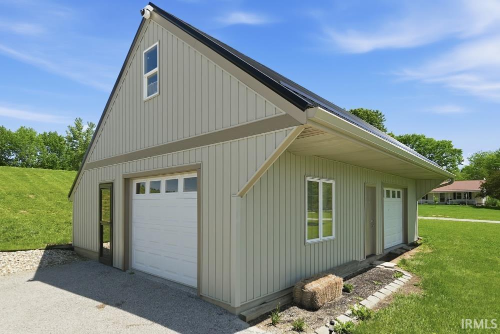 Detached garage structure featuring vertical siding, a steeply pitched dark roof, and multiple garage doors