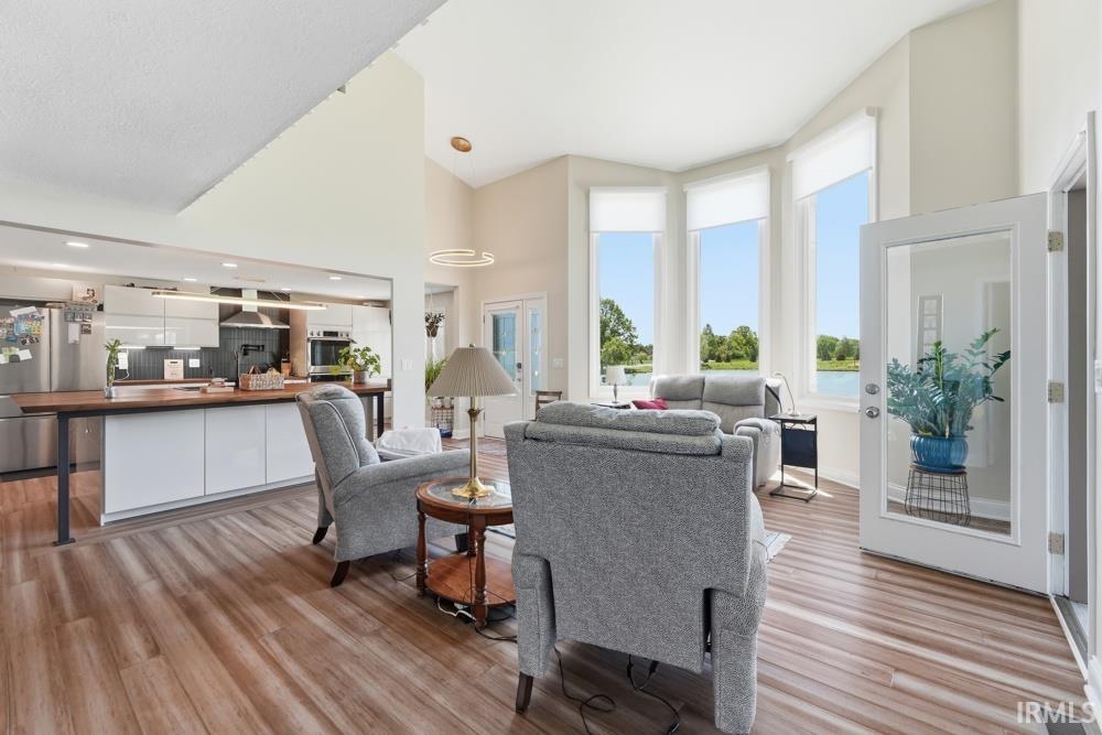 Open-concept interior featuring wood-finish flooring, a kitchen island with white cabinetry, stainless steel appliances, and a vaulted ceiling