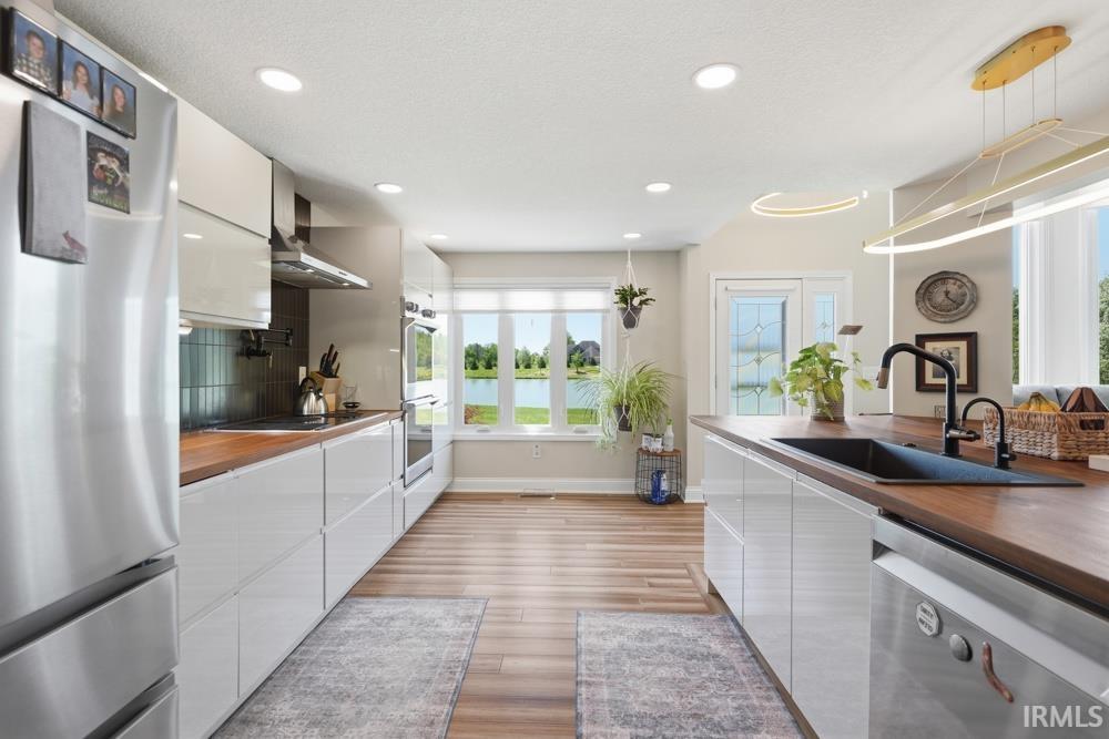 Contemporary kitchen featuring wood-finish flooring, white flat-panel cabinetry, stainless steel appliances, and wood countertops