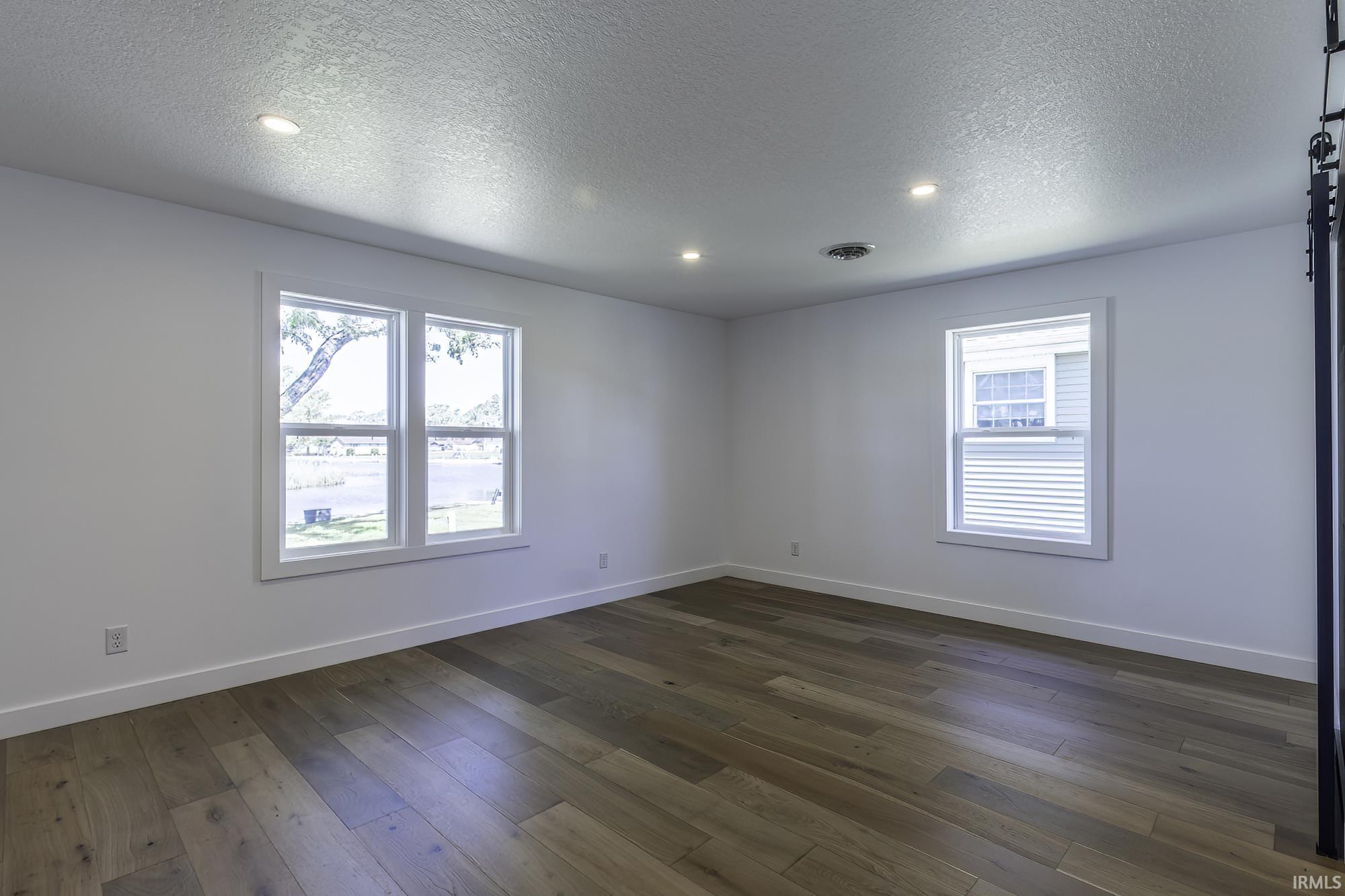 Spacious room featuring wood-finish flooring and recessed ceiling lighting