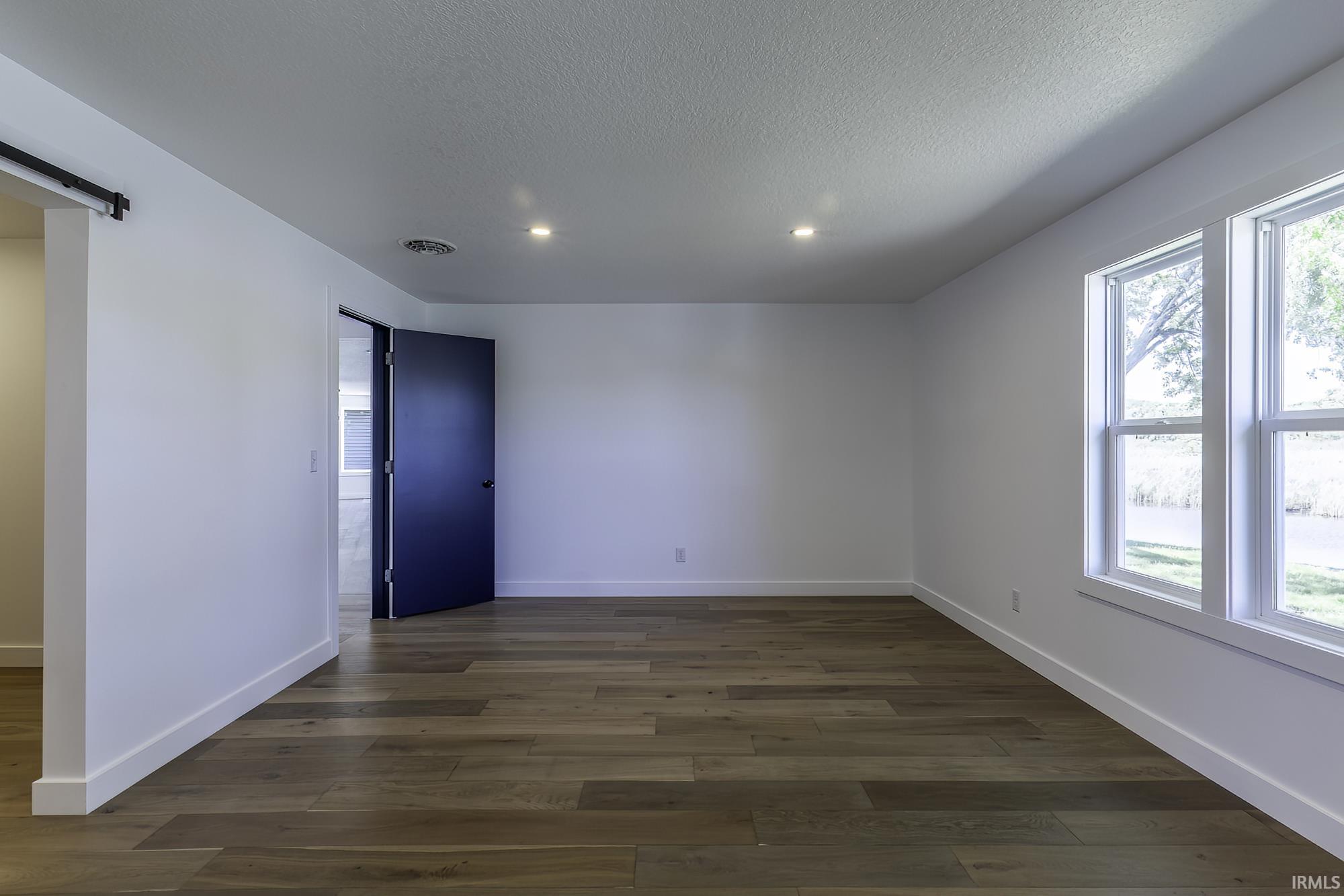 Spacious room featuring wood-finish flooring, recessed lighting, and white baseboards
