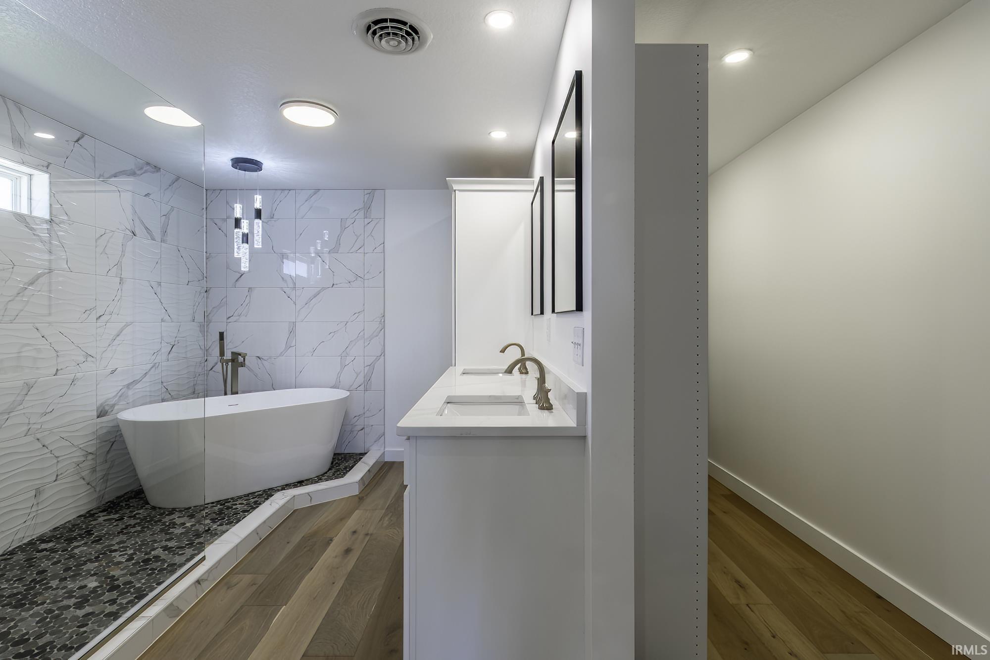Freestanding soaking tub within a glass-enclosed shower featuring a dark pebble floor