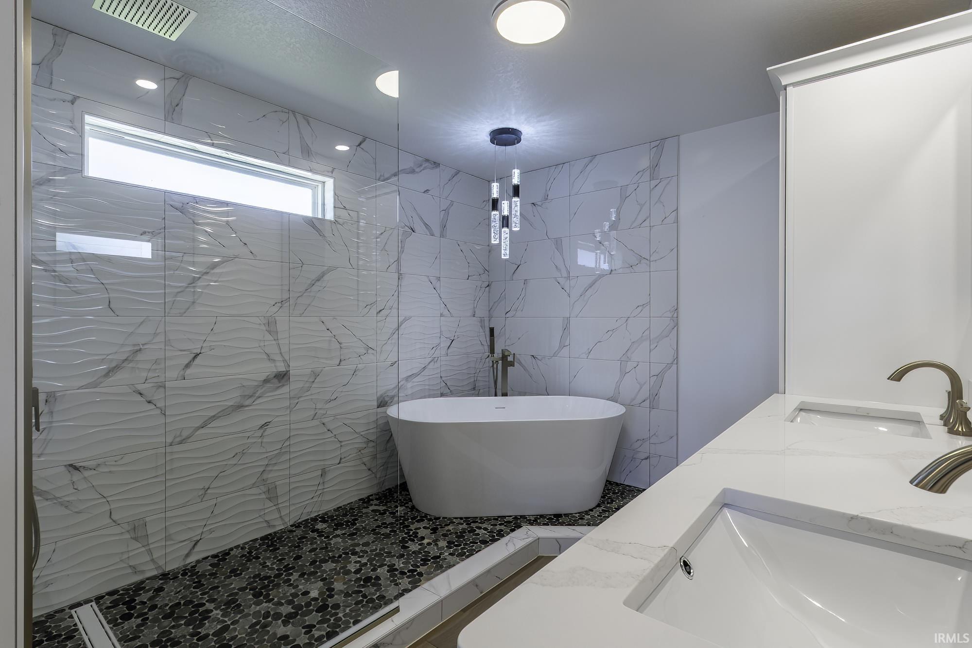 Modern bathroom featuring a freestanding tub, glass-enclosed shower with pebble flooring, and dual undermount sinks with quartz countertops