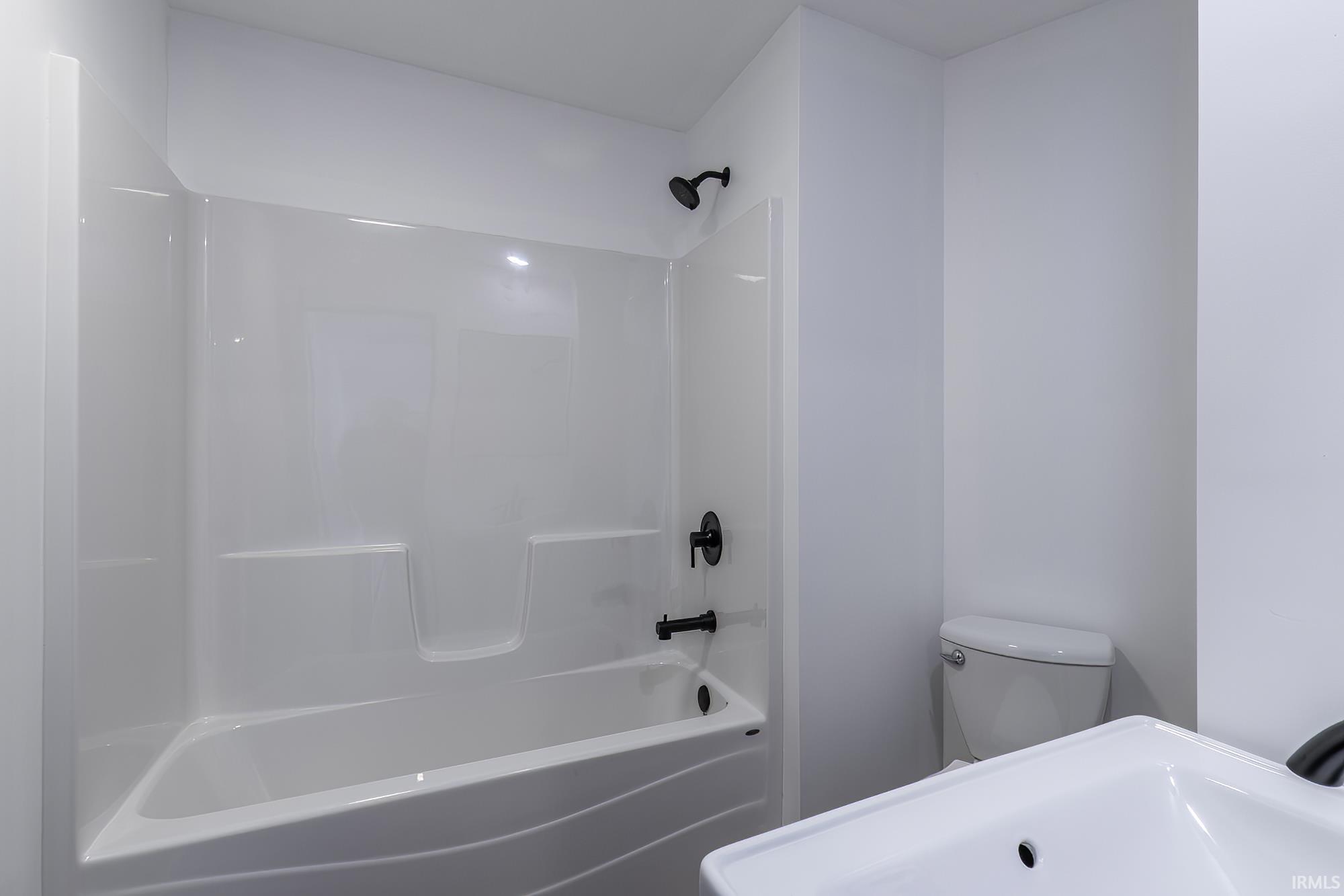 Bathroom featuring a white tub-shower combination with matte black fixtures, a white toilet, and a white vanity with an integrated sink