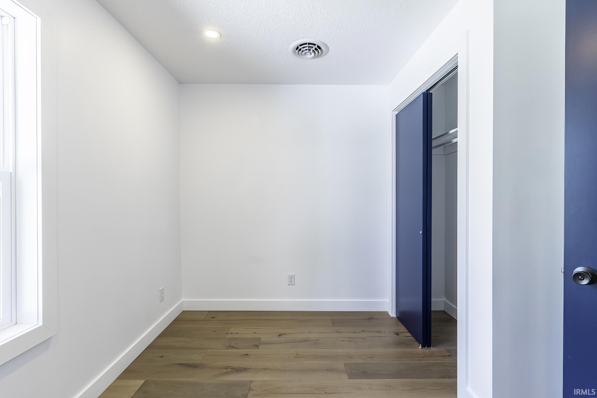 Room featuring wood-finish flooring, white baseboards, a window with white trim, recessed lighting, and a closet with bifold doors