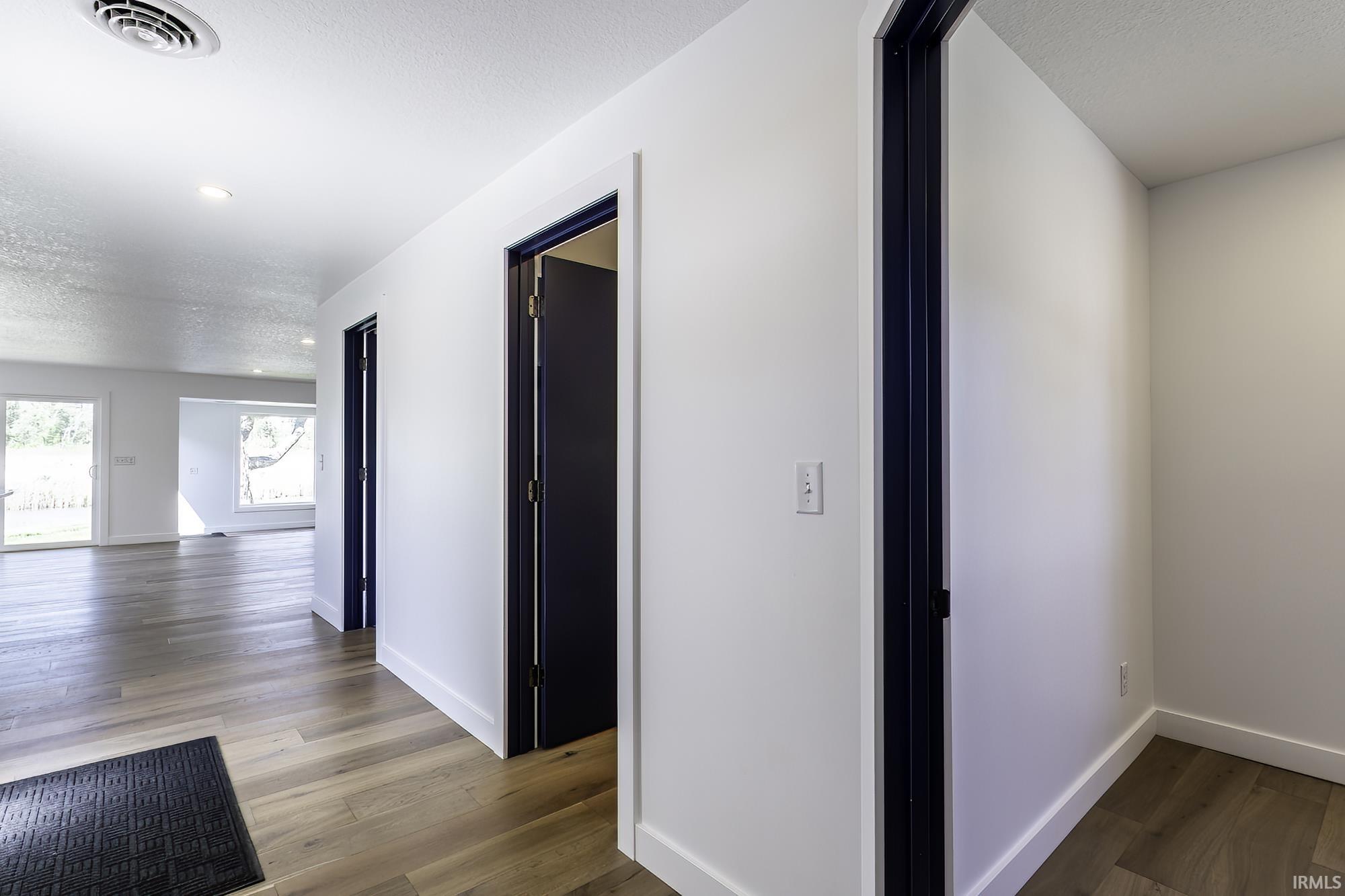 Hallway featuring wood-finish flooring, white walls, and dark-framed doorways