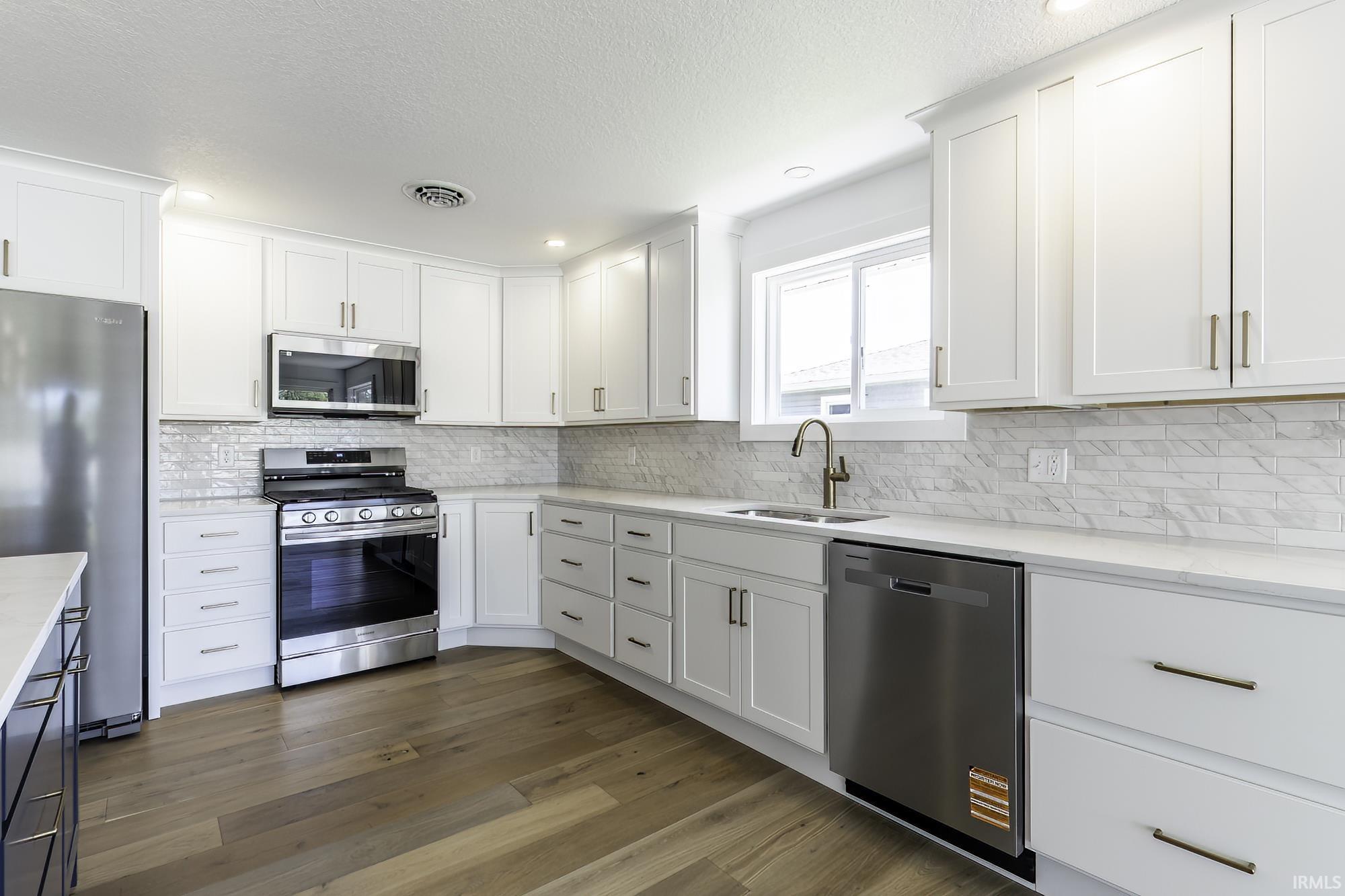 Kitchen featuring white shaker-style cabinetry, stainless steel appliances, a white tile backsplash, light-toned countertops, and wood-finish flooring