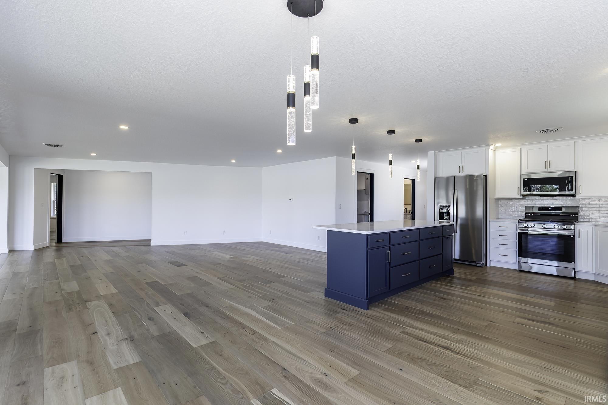 Open-concept living space featuring wood-finish flooring, recessed lighting, and a kitchen with white cabinetry