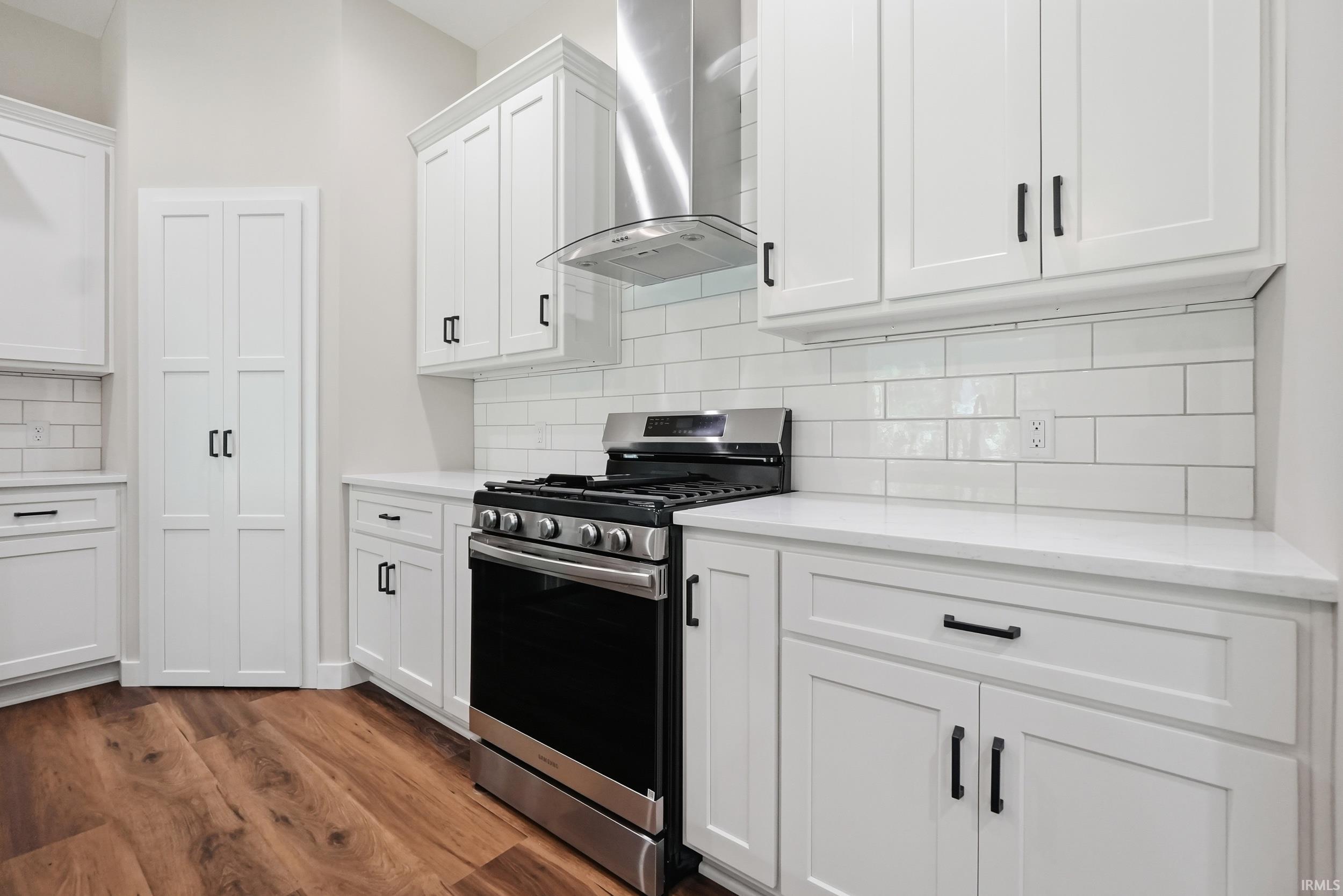 Contemporary kitchen featuring white cabinetry with dark hardware, a stainless steel range with matching range hood, and a white subway tile backsplash