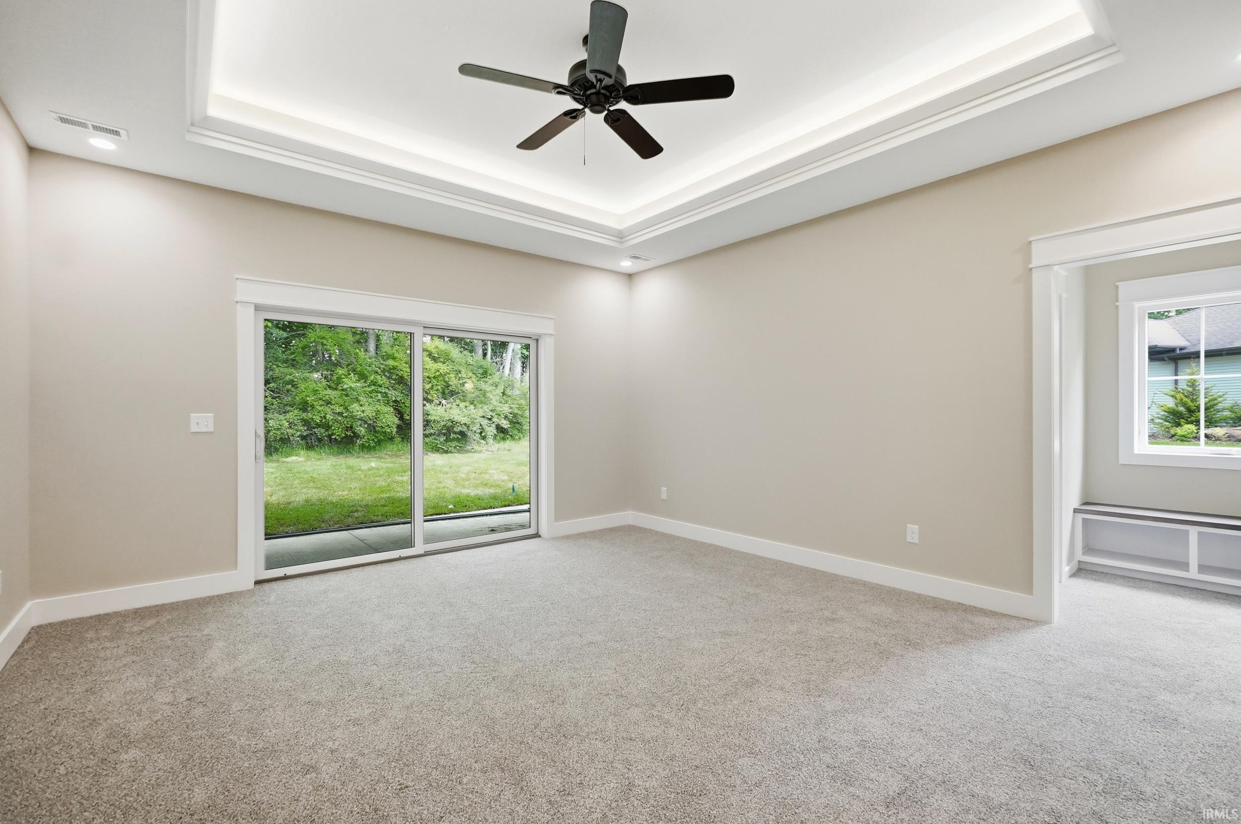 Spacious interior featuring a sliding glass door, tray ceiling with ambient lighting, recessed ceiling lights, and a ceiling fan