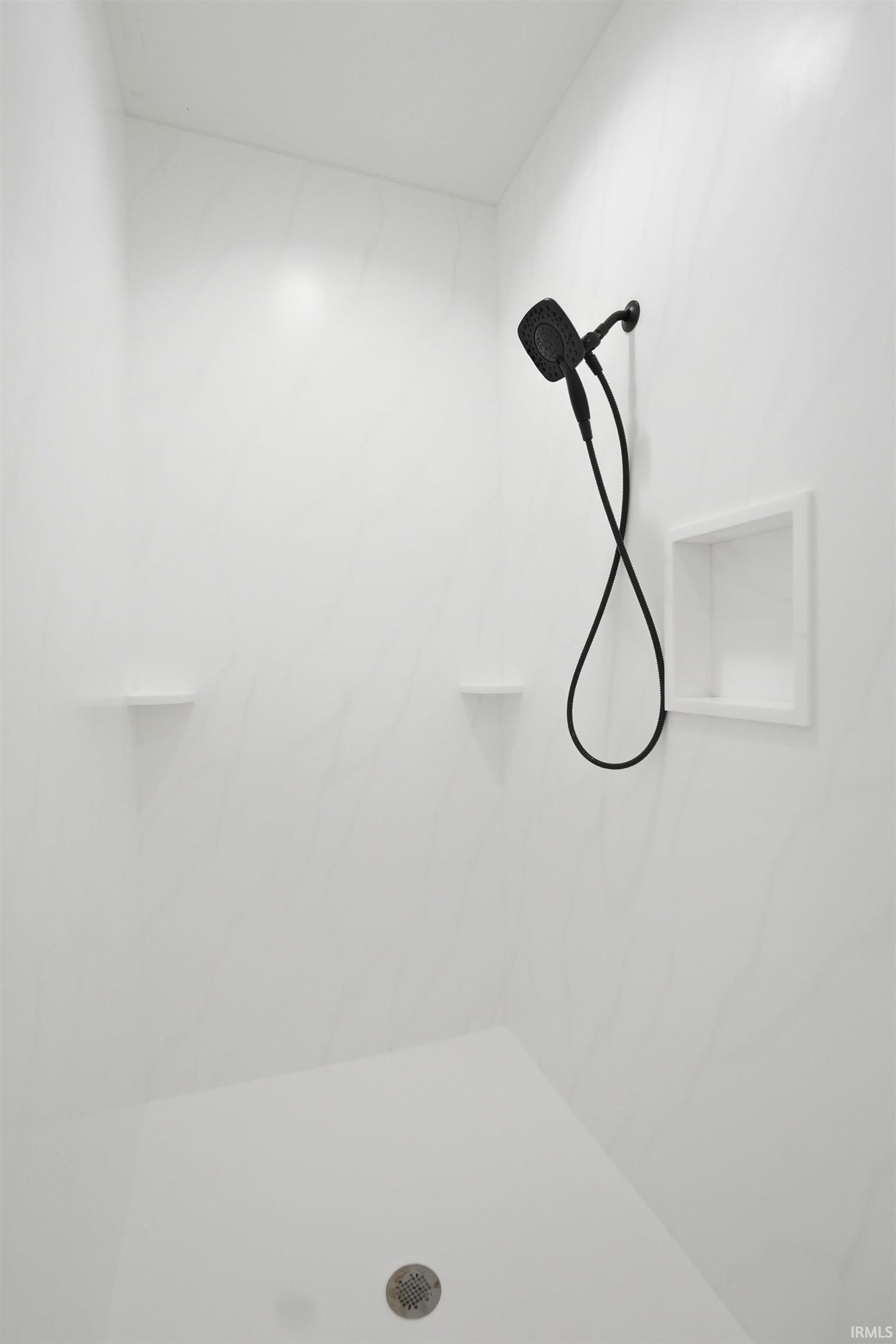 Walk-in shower featuring a matte black showerhead, integrated recessed niche, and two corner shelving units