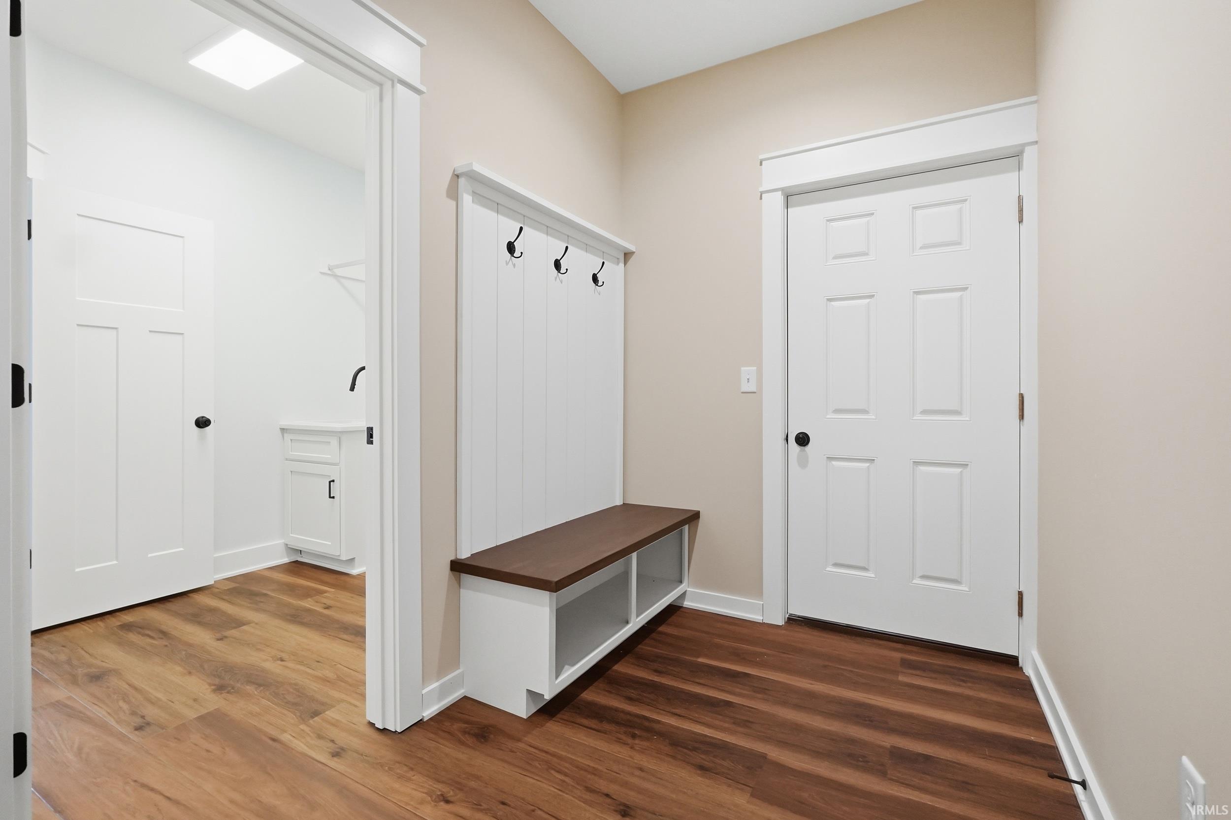 Built-in mudroom bench with storage and coat hooks, wood-finish flooring, white panel doors, and neutral wall tones