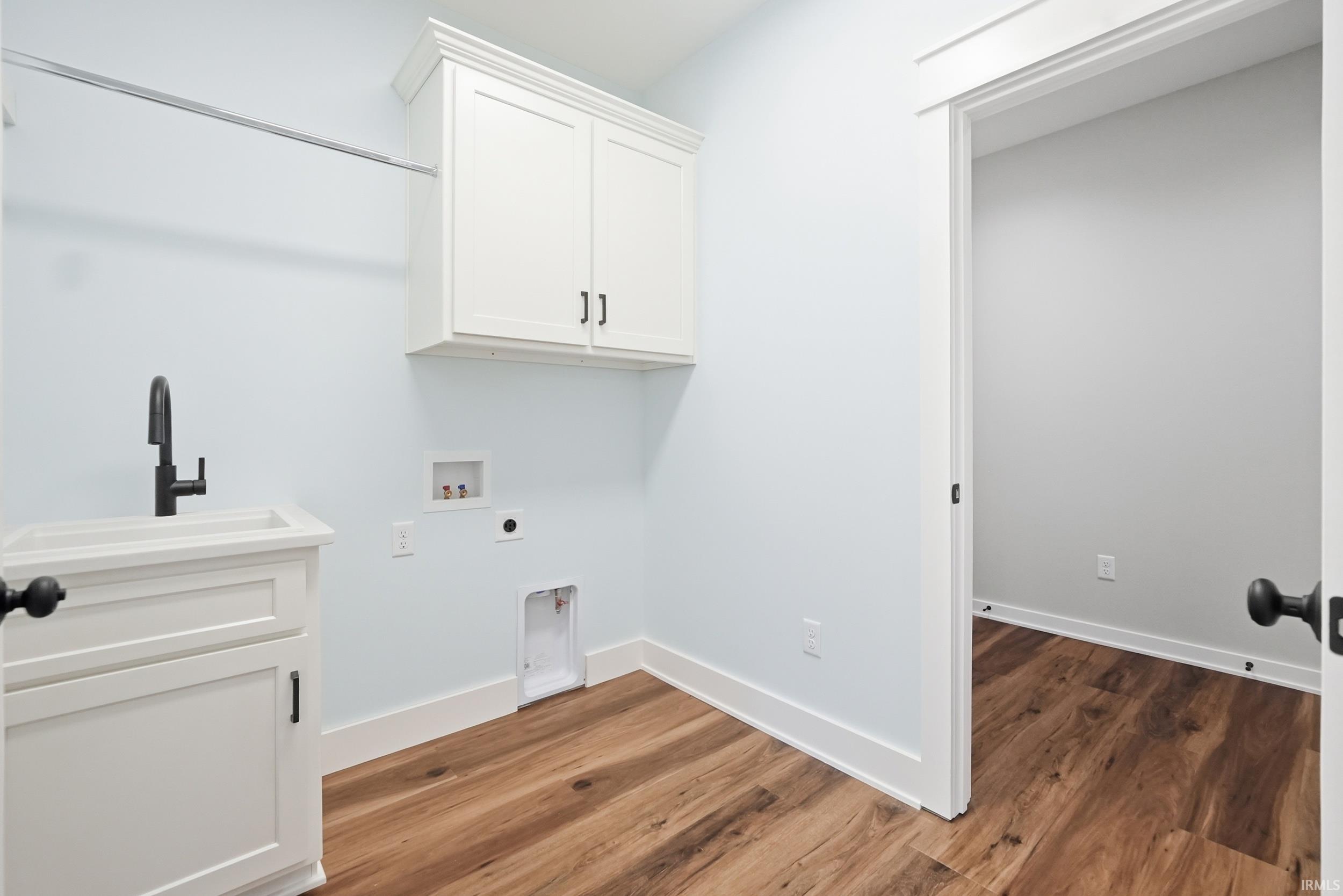 Laundry area with wood-finish flooring, white cabinetry, a utility sink with a matte black faucet, a clothing rod, and a bright interior