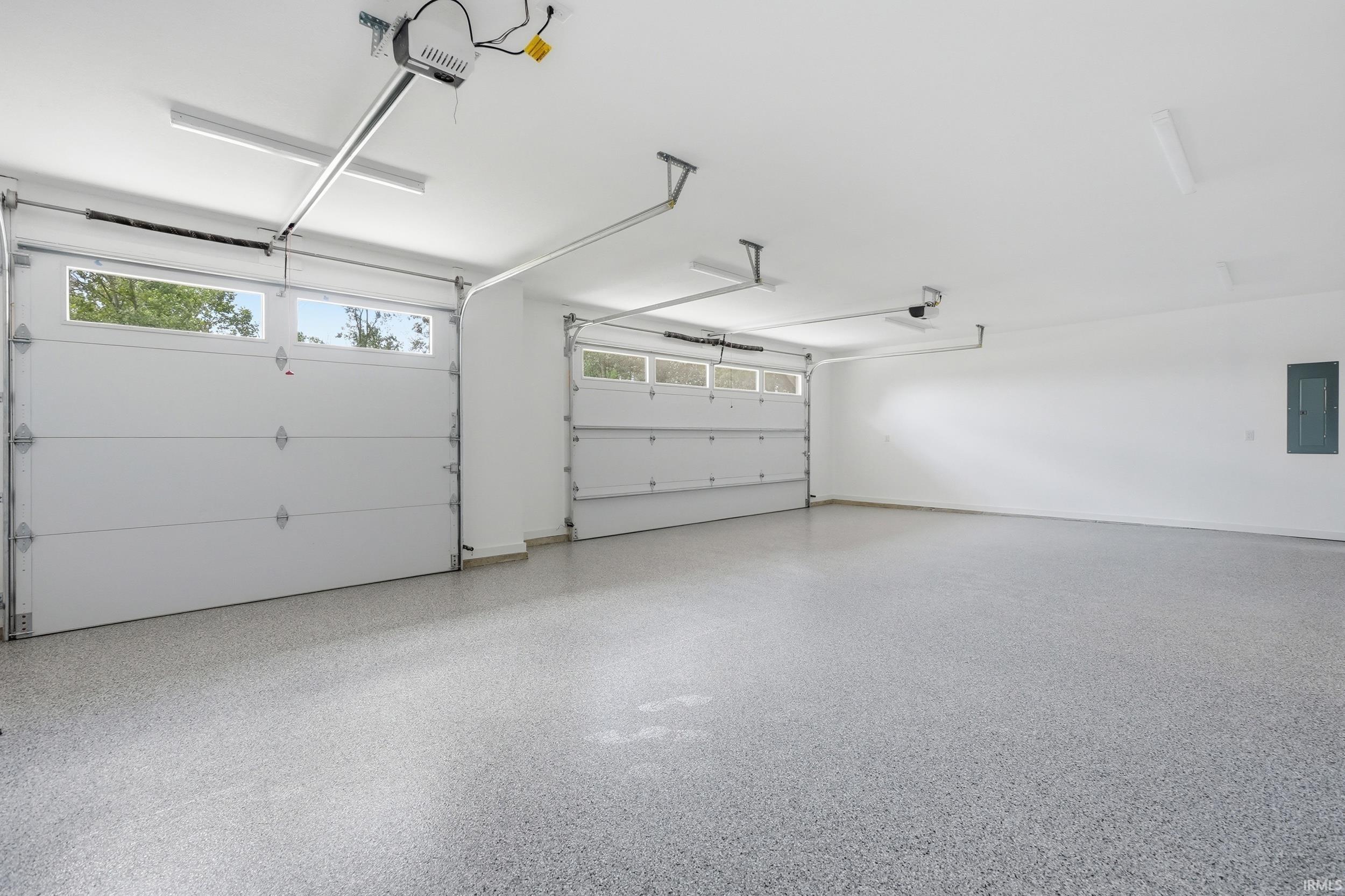 Spacious garage featuring two overhead doors with window panels, a durable speckled epoxy floor finish, clean white walls, and multiple ceiling-mounted fluorescent light fixtures