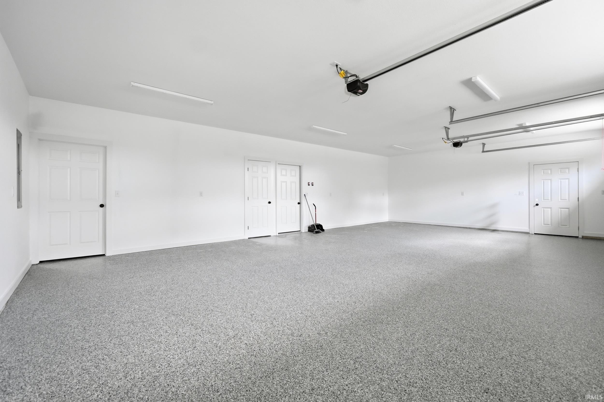 Expansive garage space featuring a speckled epoxy floor finish, multiple white paneled doors, and overhead fluorescent lighting fixtures