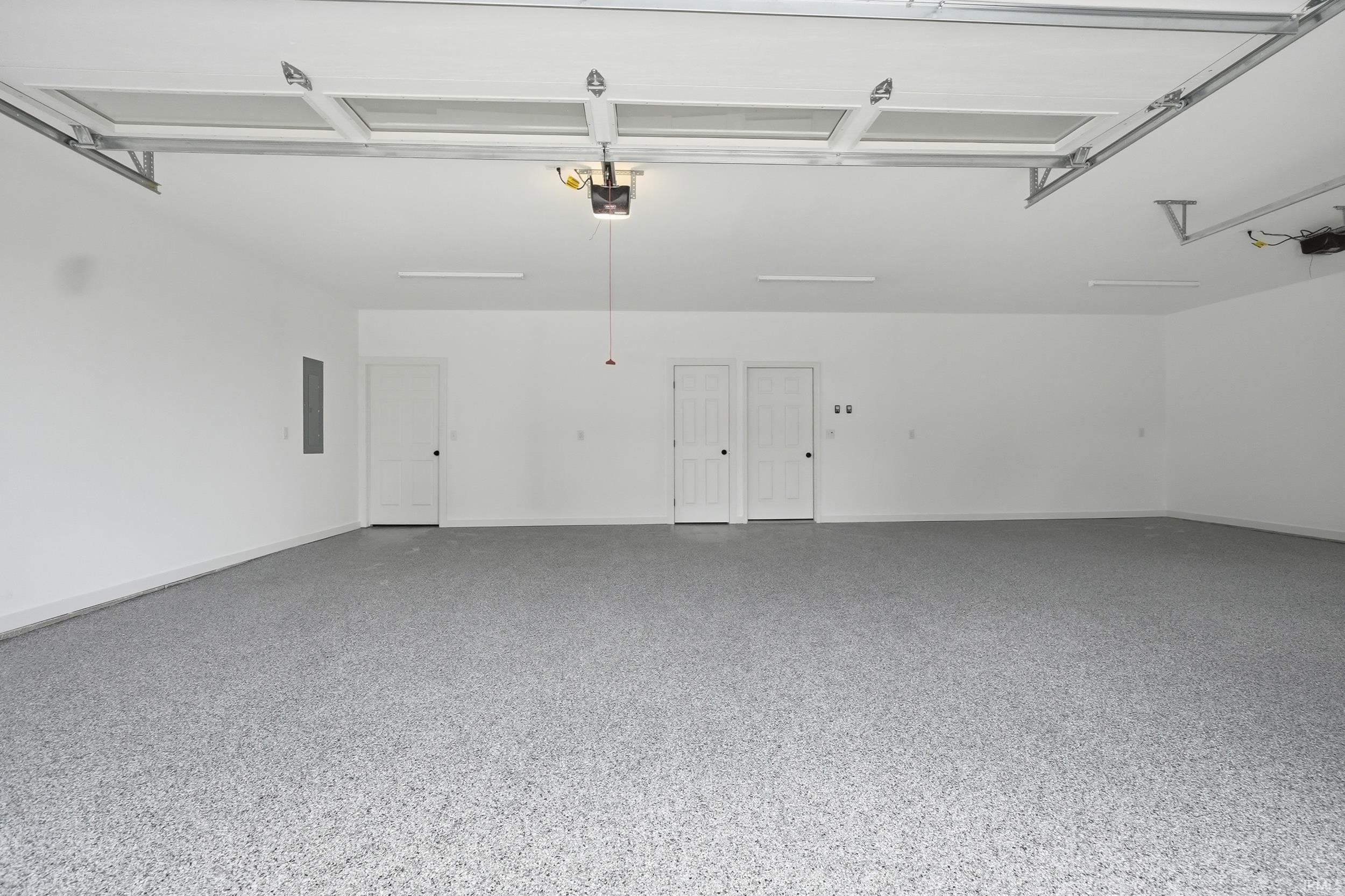 Spacious garage featuring a speckled epoxy floor, white painted walls, and multiple access doors