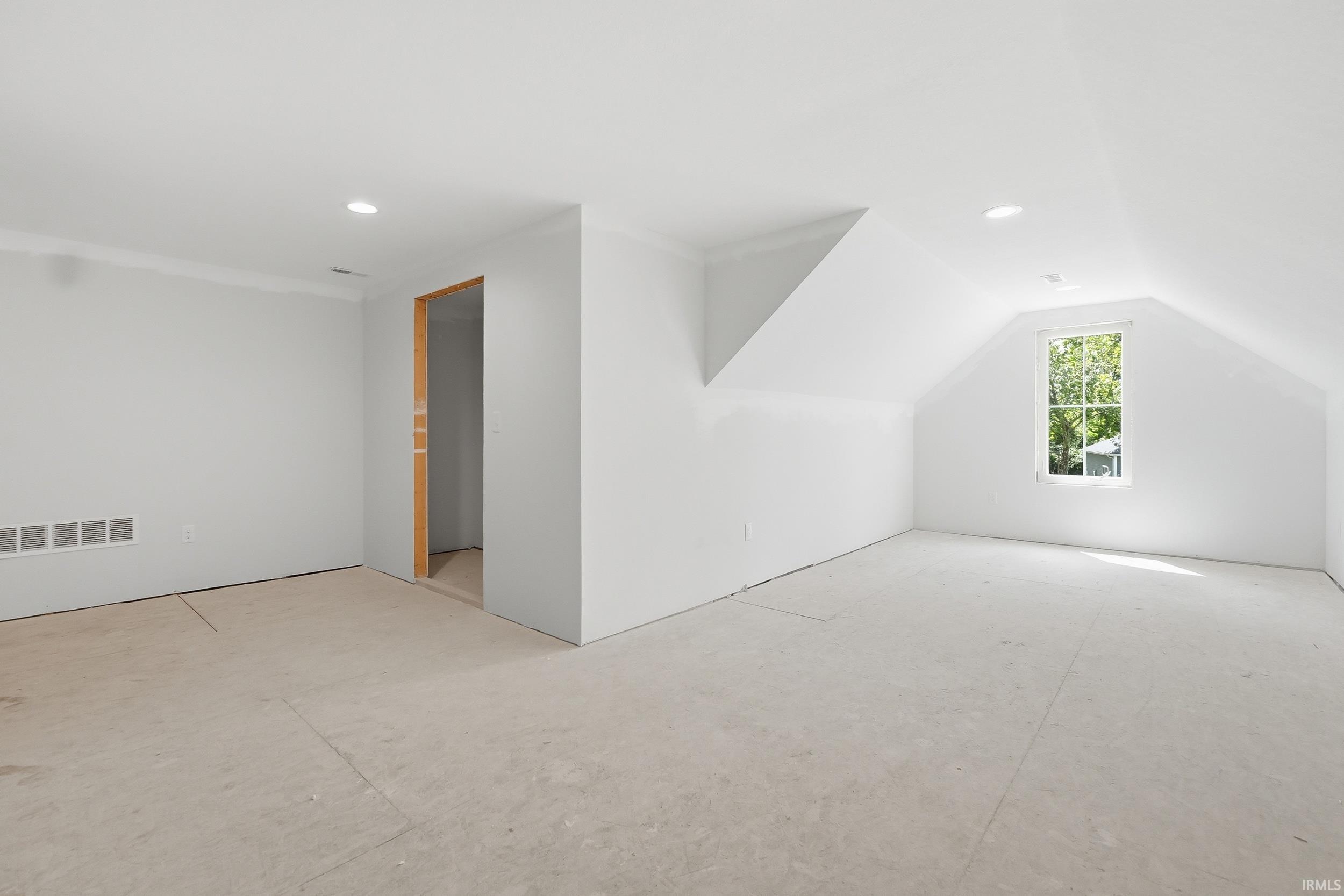 Spacious room with white walls and sloped ceilings, featuring recessed lighting, a single window, and an open doorway