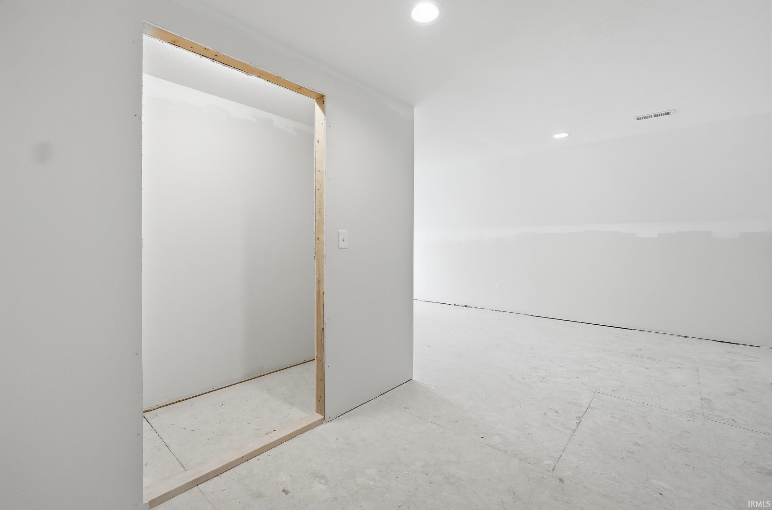 Unfinished interior space featuring recessed lighting, a framed doorway, white walls, and light-colored flooring