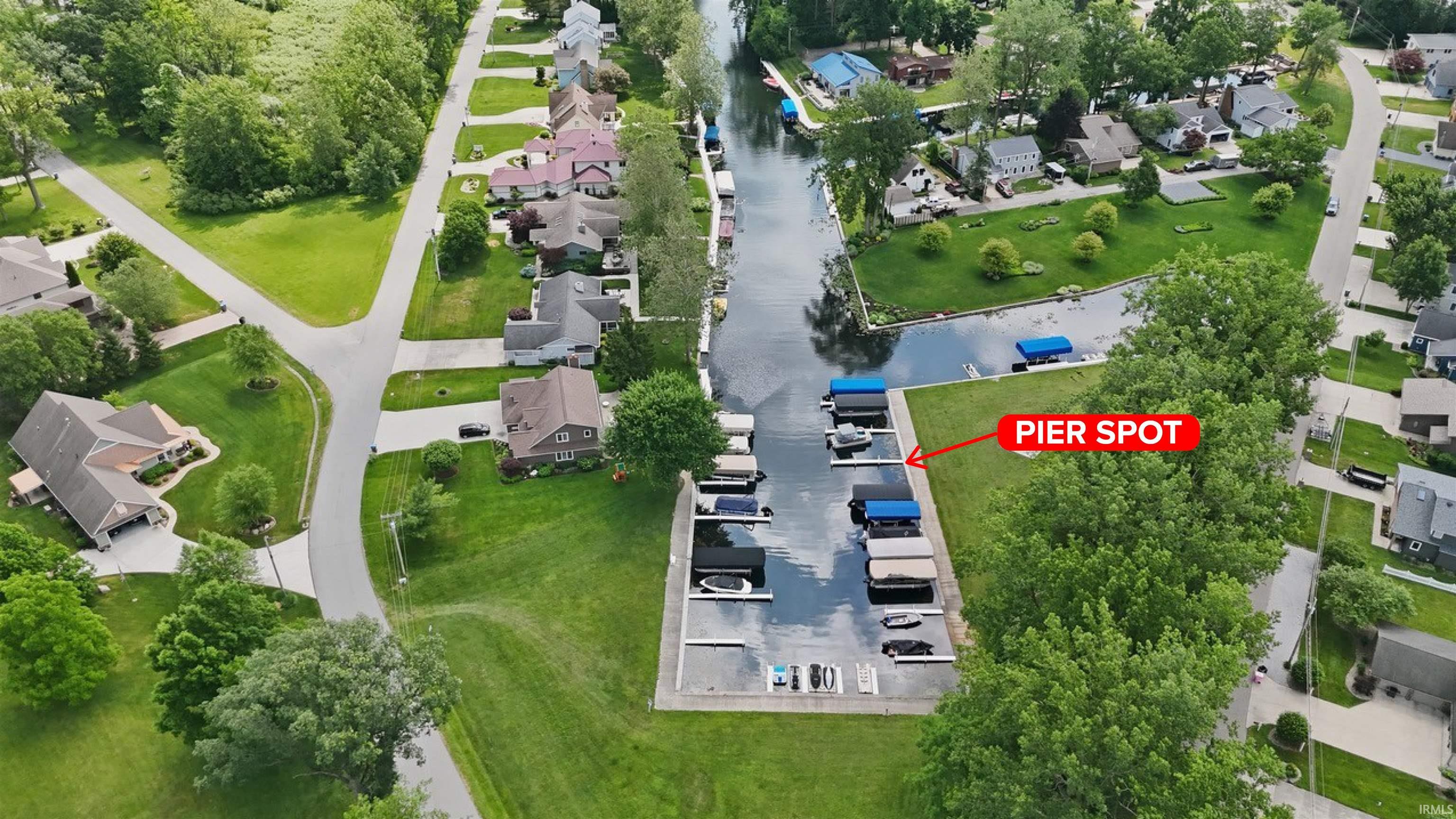 Waterfront property featuring a private pier spot, paved roadways, mature trees, and a manicured lawn