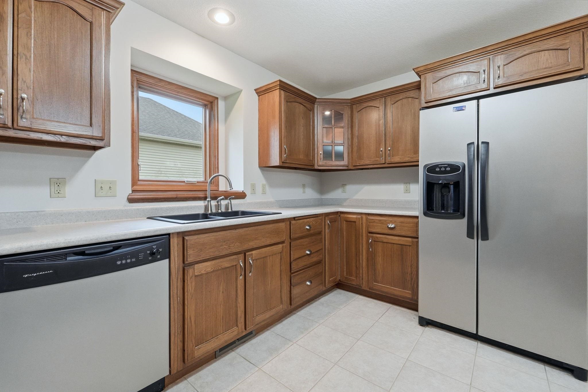 Kitchen featuring wood cabinetry, white countertops, tile flooring, a stainless steel side-by-side refrigerator, and a stainless steel dishwasher