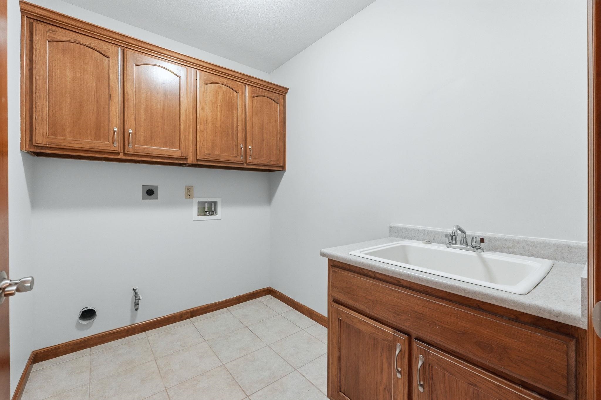 Utility room featuring a built-in sink with a countertop, wood-finish cabinetry, and ceramic tile flooring
