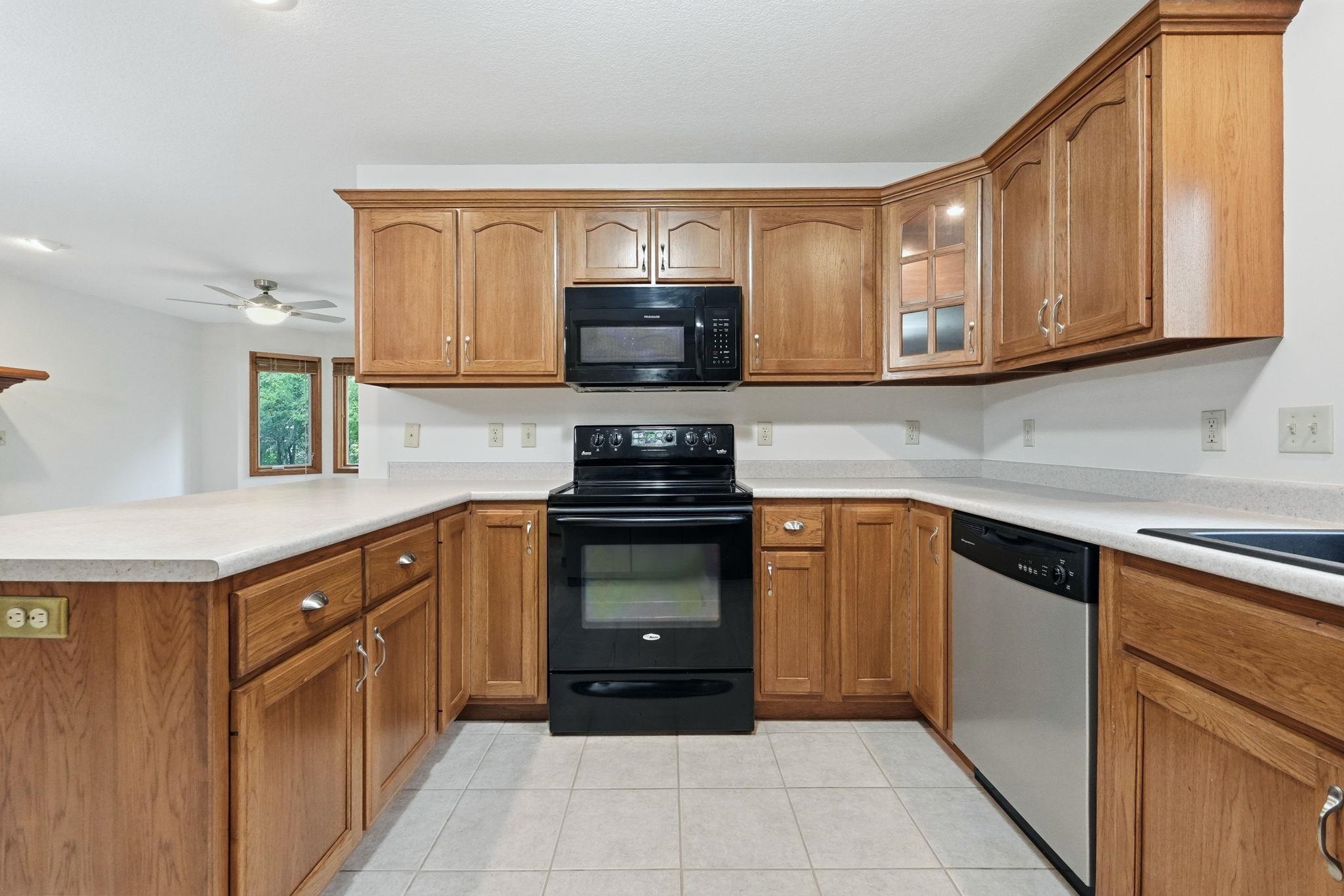 Kitchen featuring light wood cabinetry, light countertops, black appliances, a stainless steel dishwasher, and tile flooring