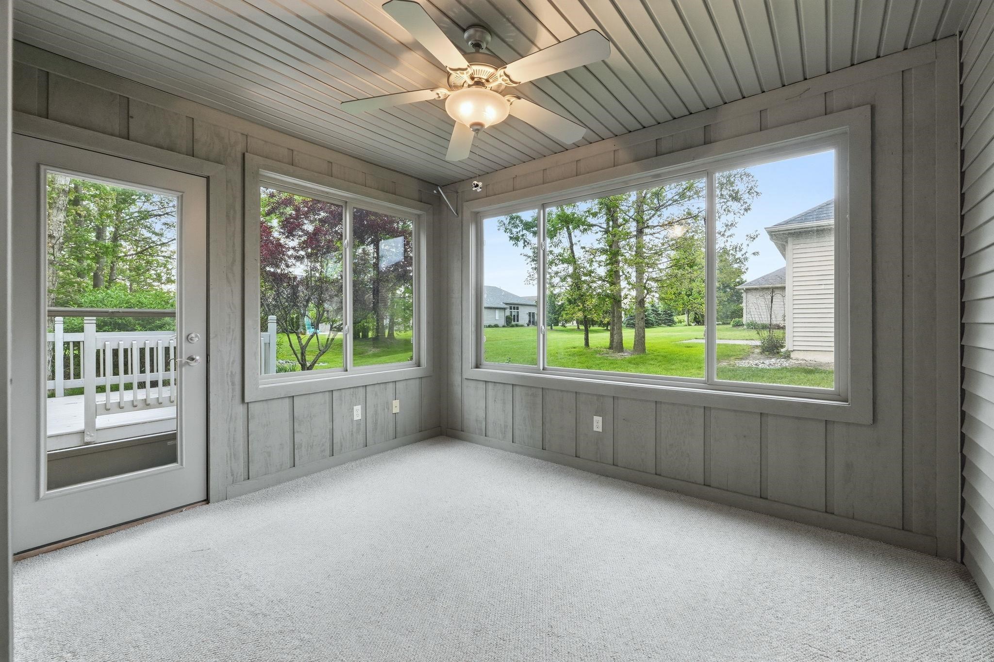 Sunroom with full-light exterior door, expansive windows, carpeted flooring, and a ceiling fan with integrated lighting