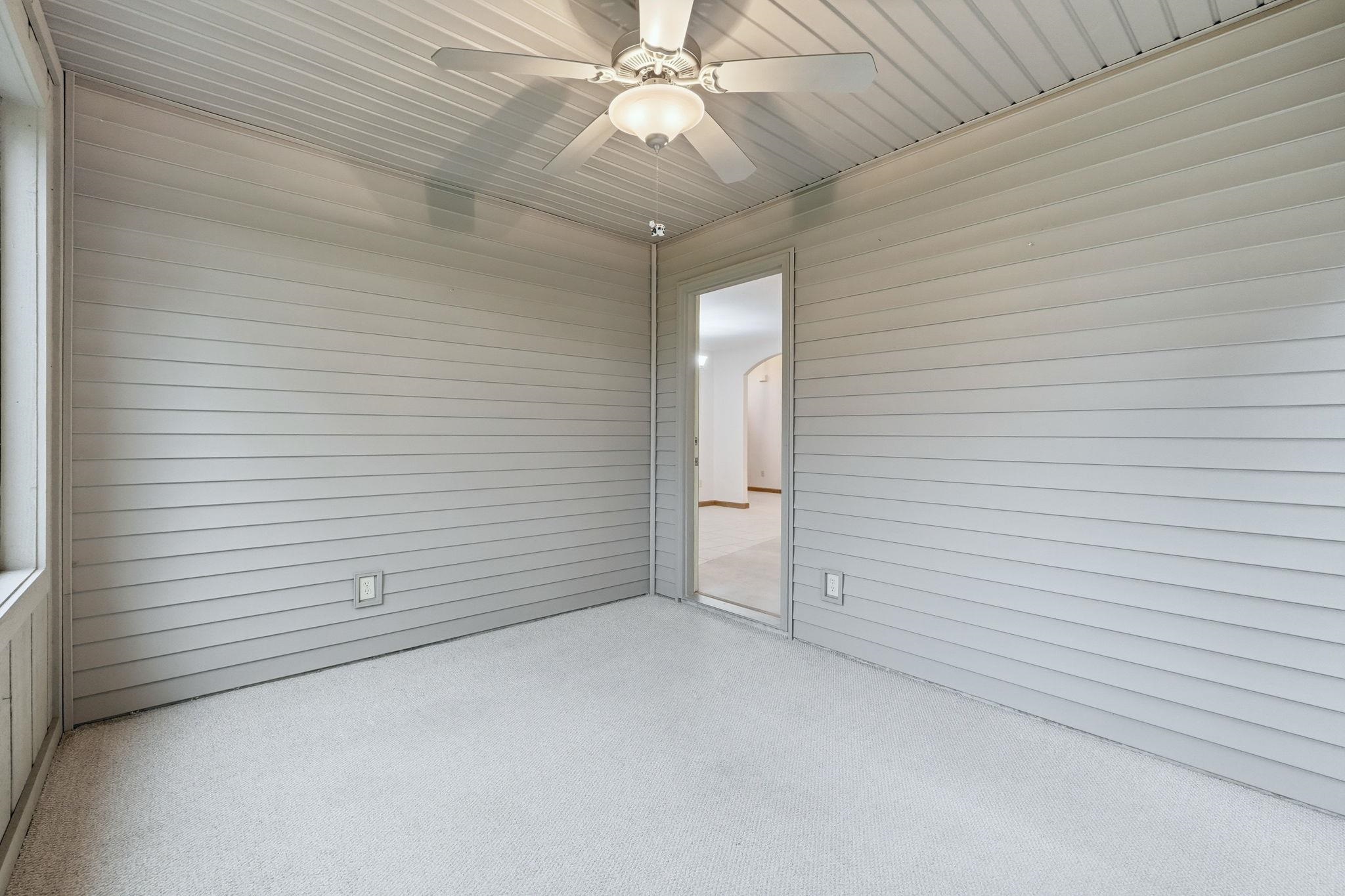 Screened-in porch featuring a ceiling fan with light fixture, horizontal panel siding, and light-toned carpet flooring