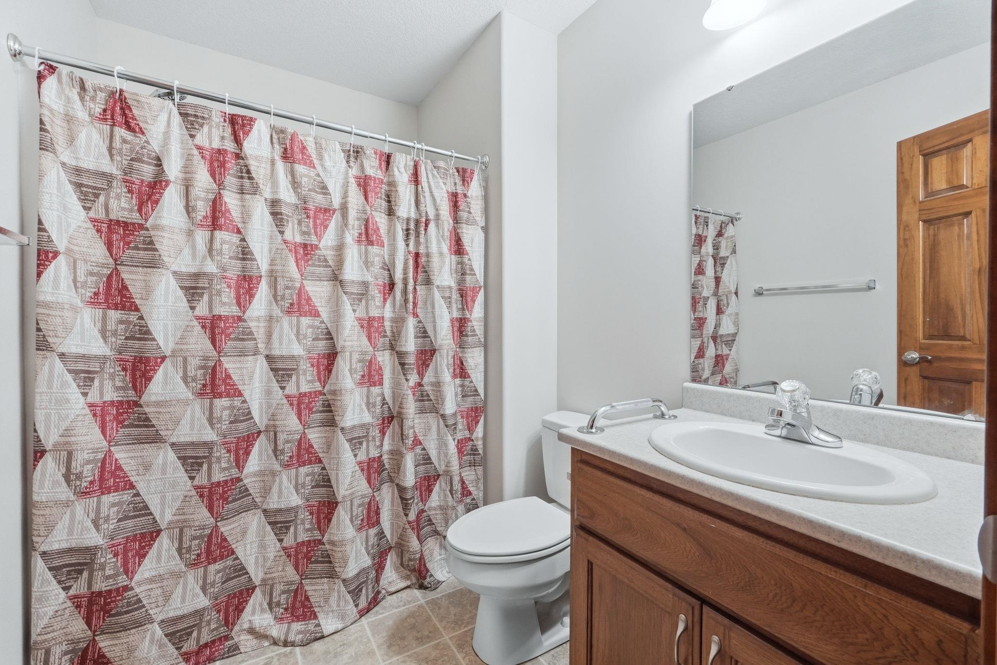 Full bathroom featuring a shower-tub combination, a wood-finish vanity with an integrated sink, a large wall-mounted mirror, and tile flooring