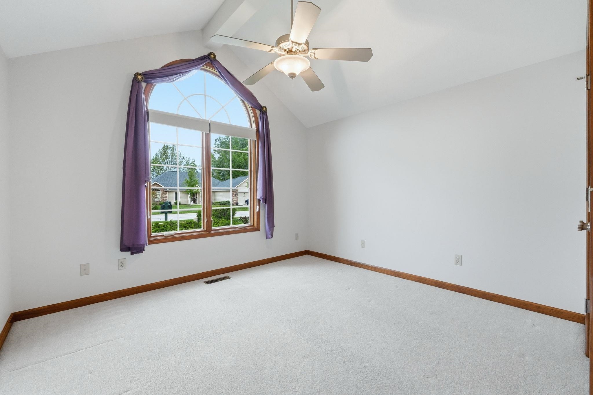 Arched window with wood trim, vaulted ceiling, ceiling fan, white wall finishes, and light-colored carpeting