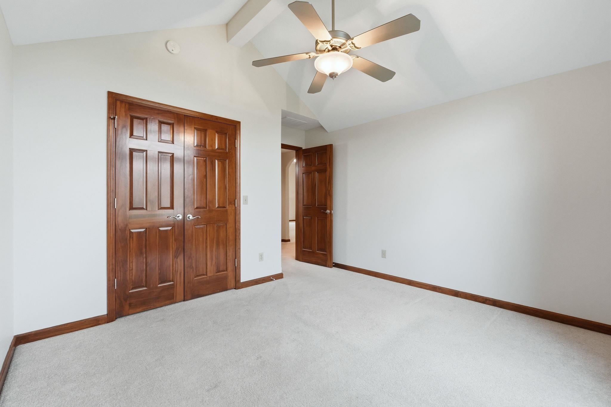 Vaulted ceiling room with white walls, light-toned carpeting, and dark wood-paneled bi-fold doors