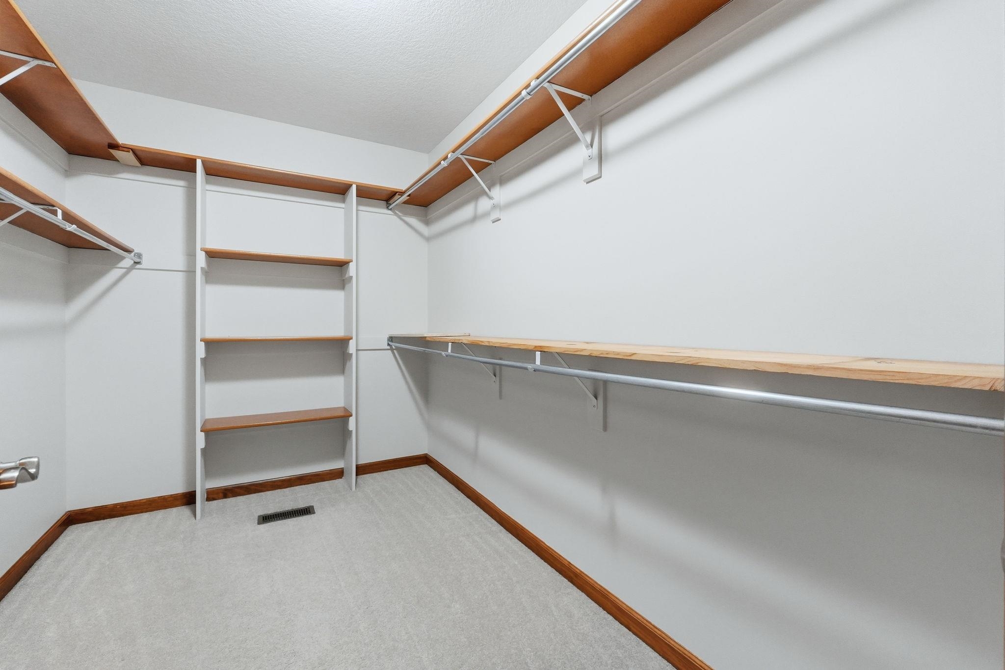 Walk-in closet with light gray carpeting, wood-finish shelving, metal hanging rods, and white wall finishes