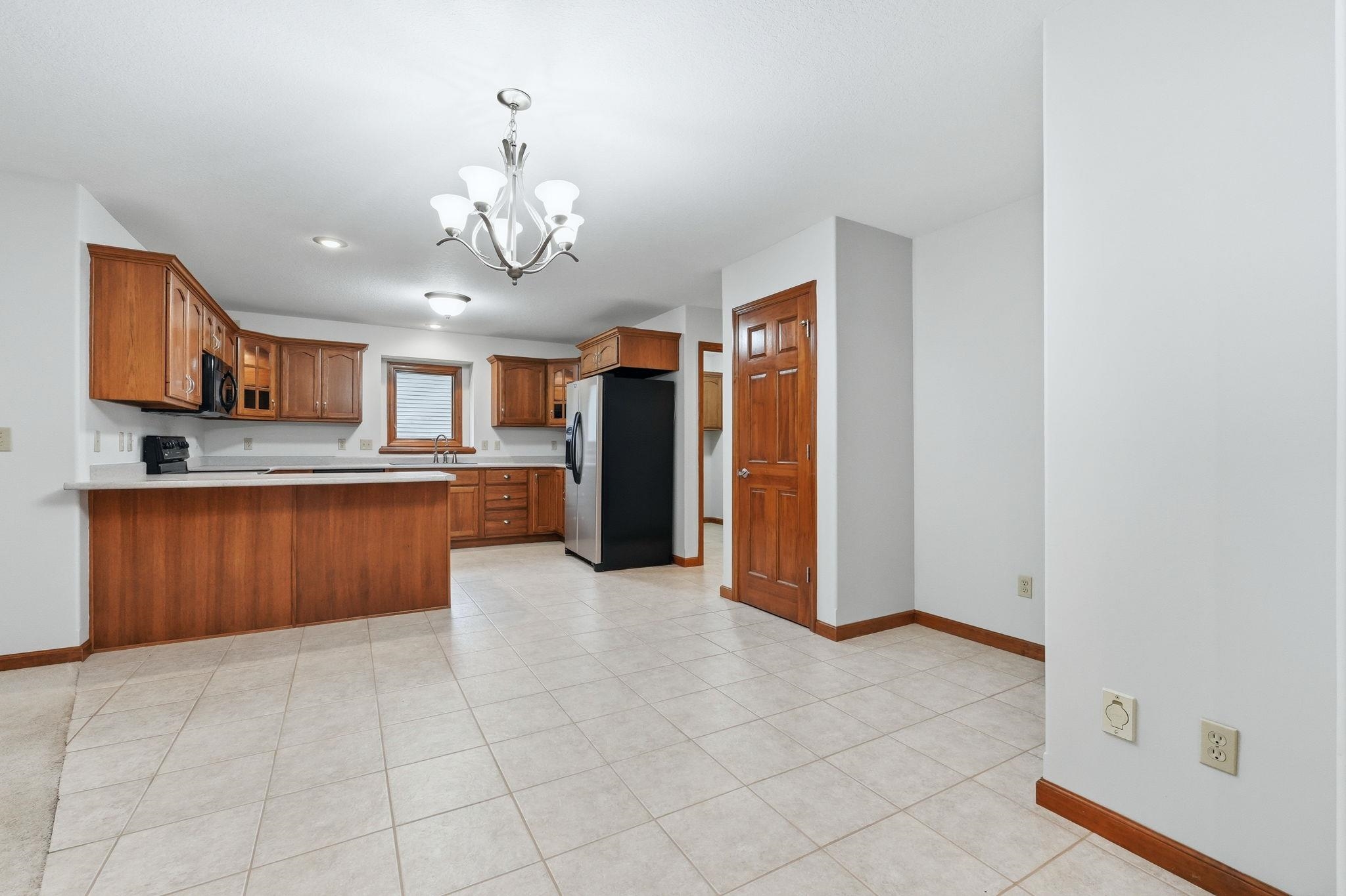 Kitchen featuring wood cabinetry, light-toned countertops, a stainless steel and black refrigerator, and tile flooring
