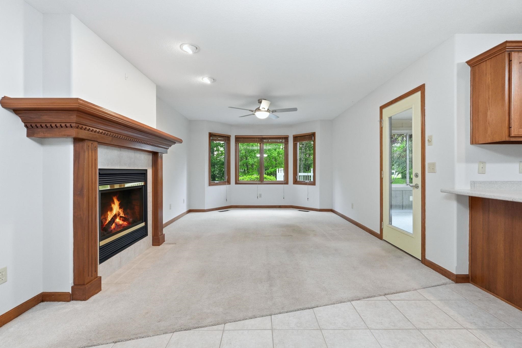 Living area featuring a prominent fireplace with a carved wood mantle, a bay window, and light-toned carpet