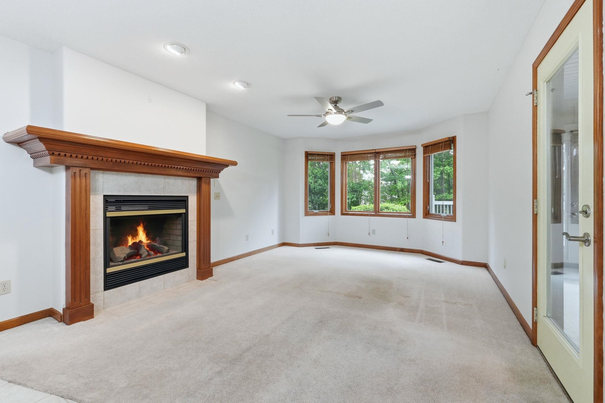 Spacious interior featuring a gas fireplace with a wood-mantel surround and tile hearth, a bay window with wood trim, recessed lighting, a ceiling fan, and light-toned carpeting