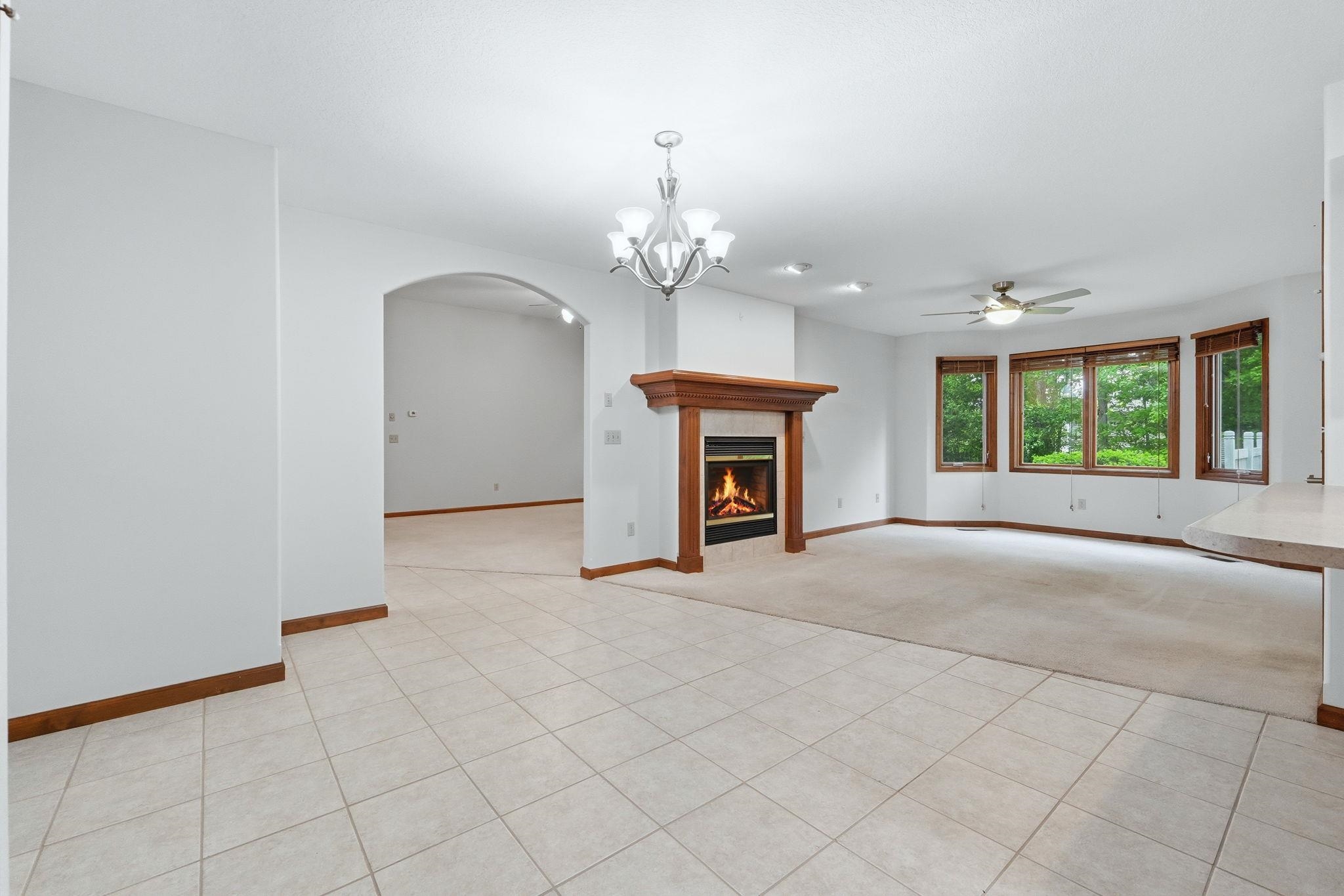 Open concept living area featuring light-toned tile flooring, a wood-mantled fireplace, and a large bay window